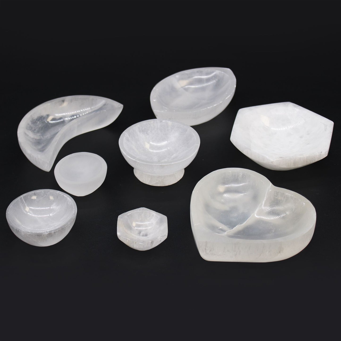 A collection of various white selenite bowls on a black background.