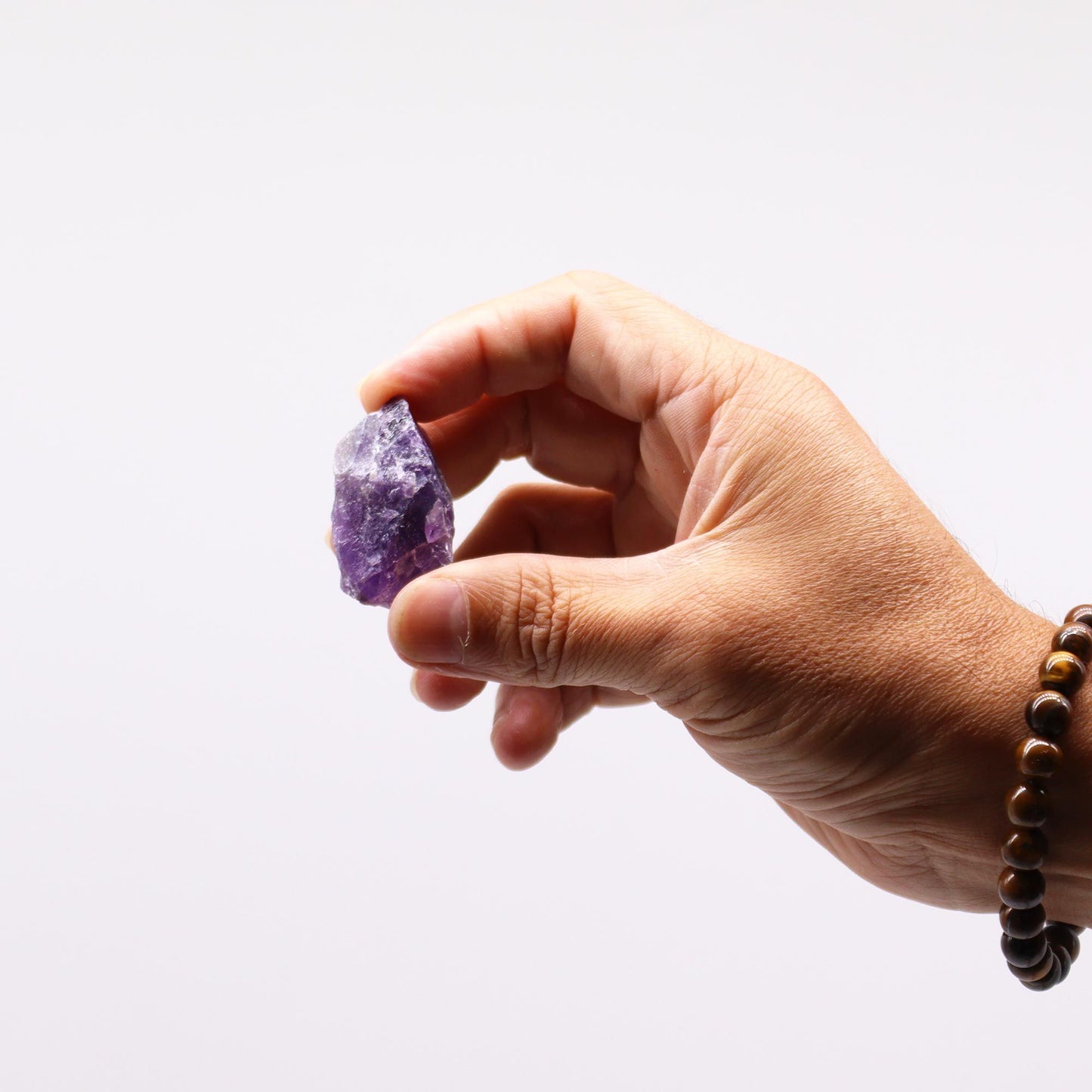 Eine Hand hält einen rohen, violetten Amethyst-Edelstein.