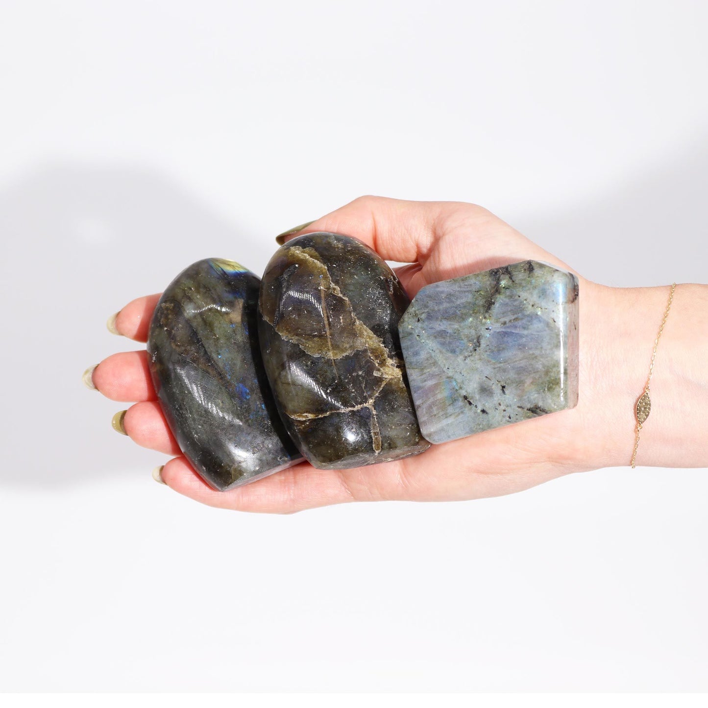 Drei große, polierte Labradorit-Trommelsteine mit blau-grüner Irisierung in einer Hand.