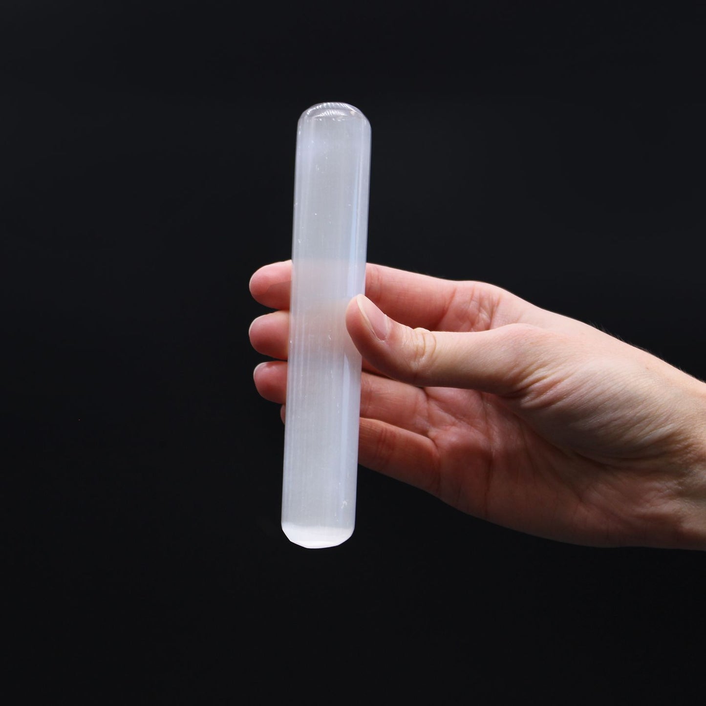Ein 16 cm langer Selenitstab mit abgerundeten Enden, der in einer Hand gehalten wird.
