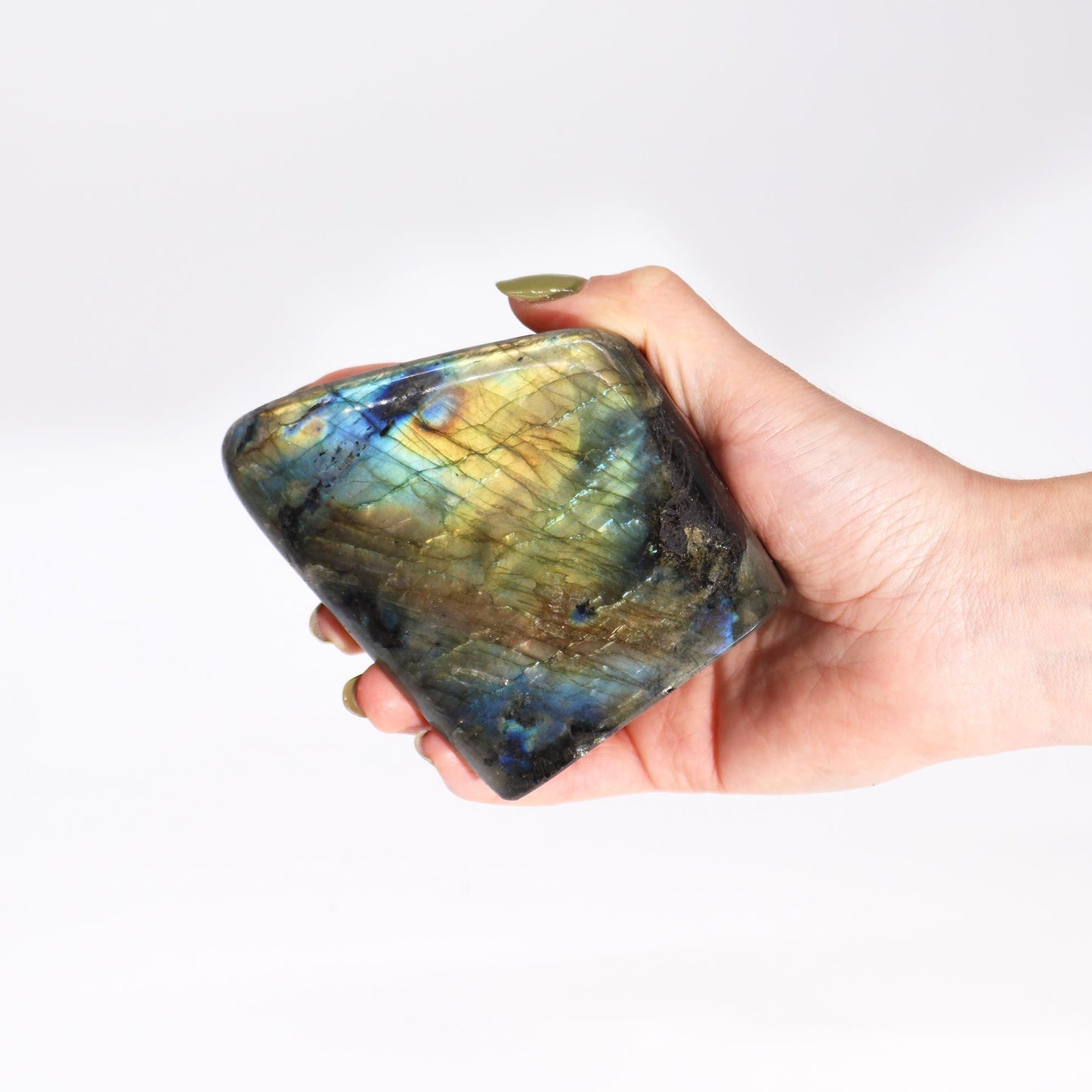 Hand hält einen großen, facettierten Labradorit mit blau-grünem Schimmer.