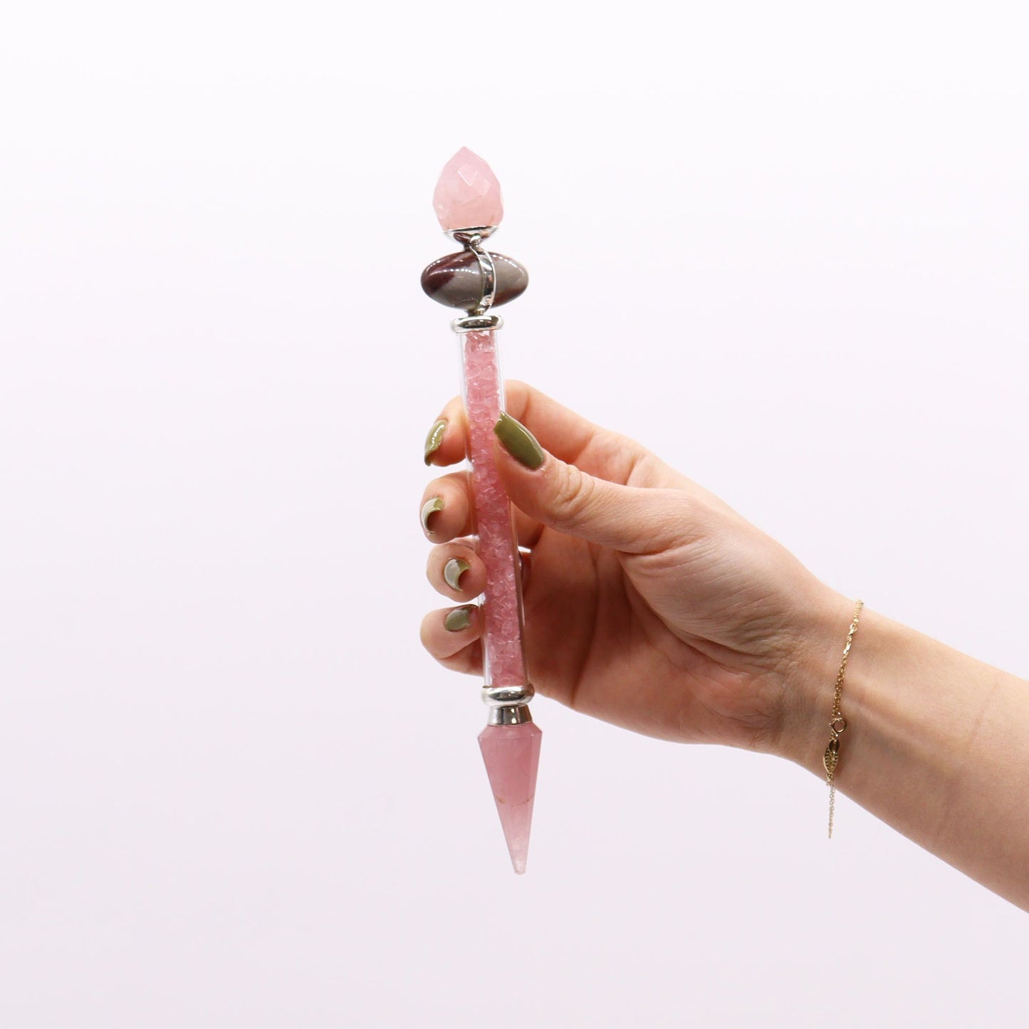 A hand holds a rose quartz and shiva lingam wand with a gold bracelet.
