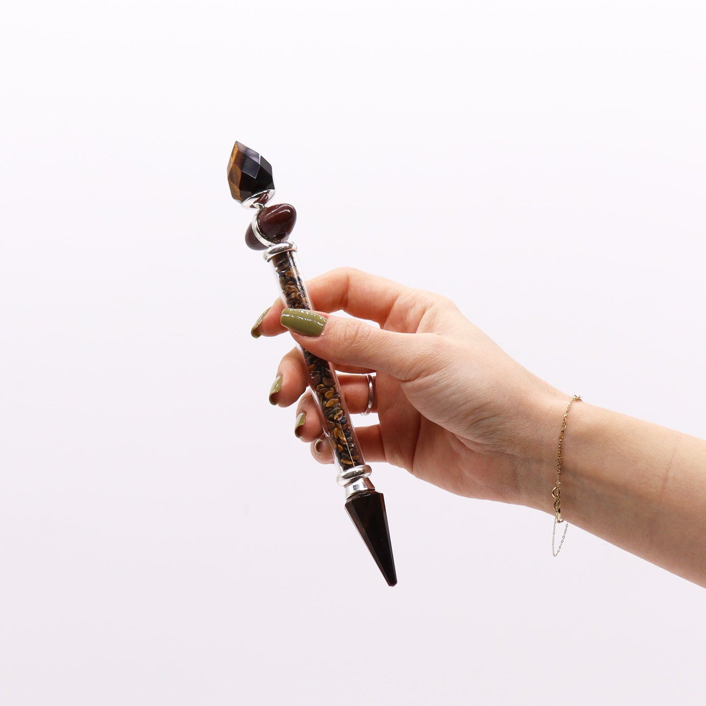 A hand holds a tiger eye and gemstone wand with a pointed tip.