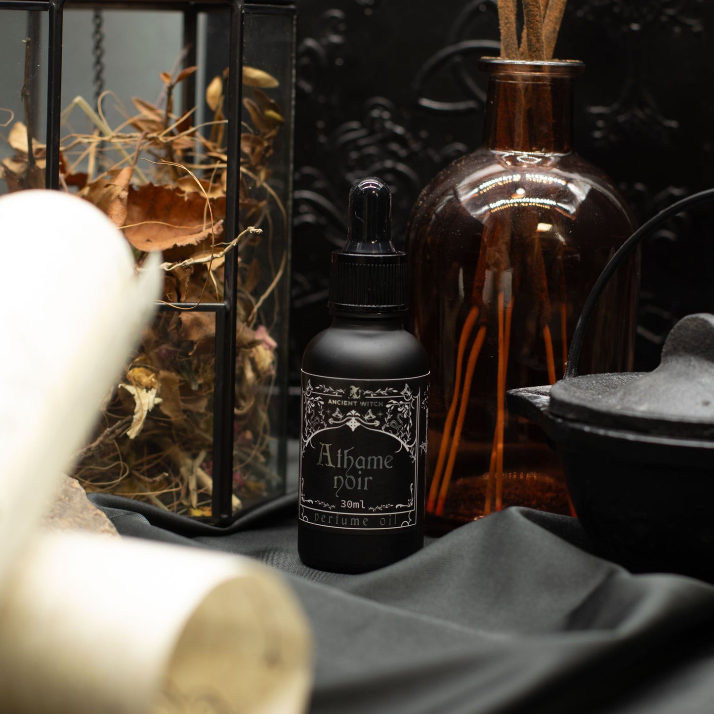 Black bottle of Athame Noir perfume oil with dried leaves and a brown glass diffuser.