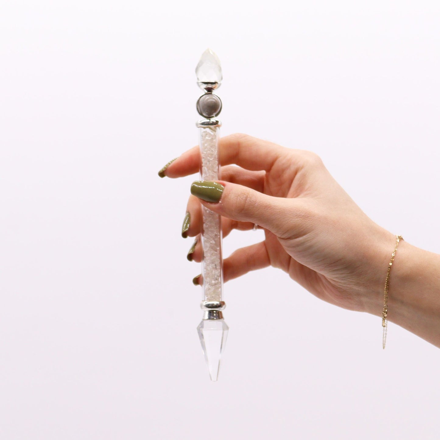 A hand holds a rock quartz Shiva Lingam magic wand with crystal chips.