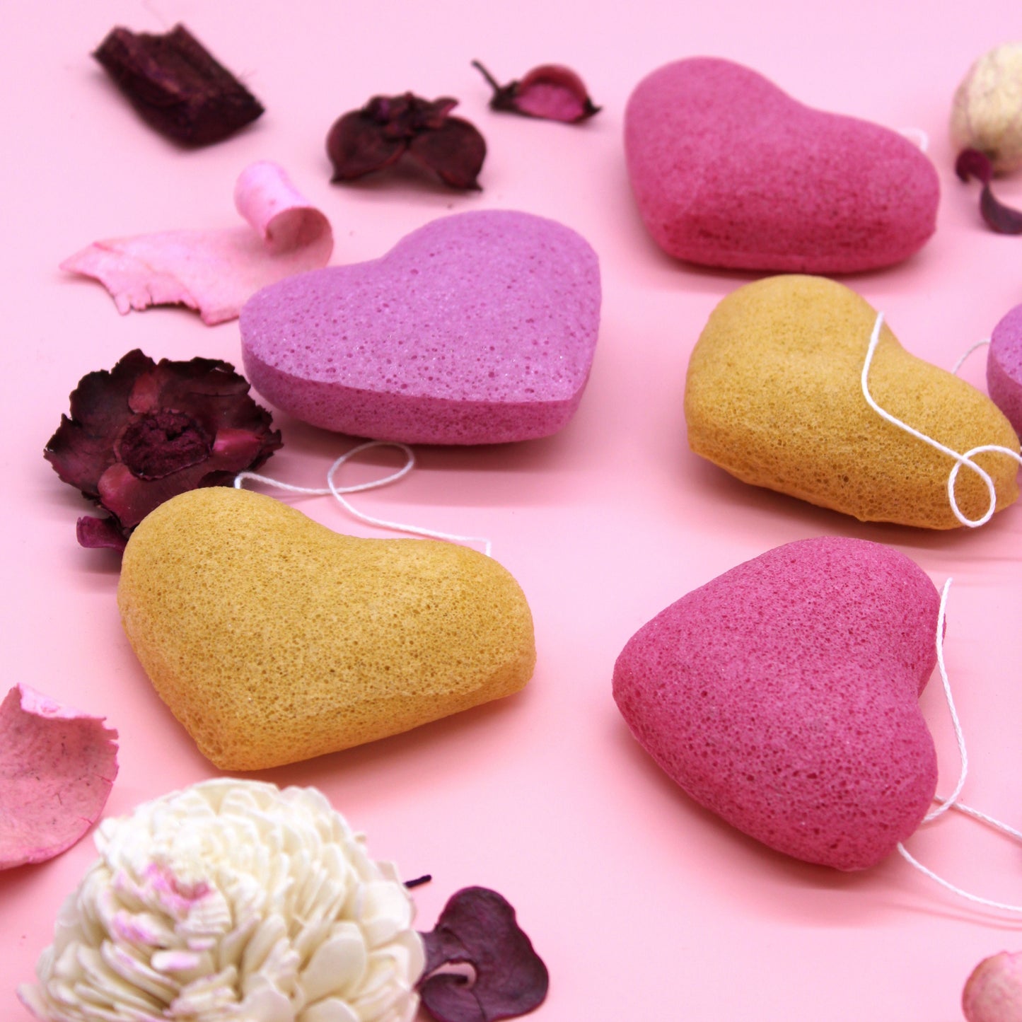 Konjac heart sponges in pink and yellow with decorative elements on a pink background.