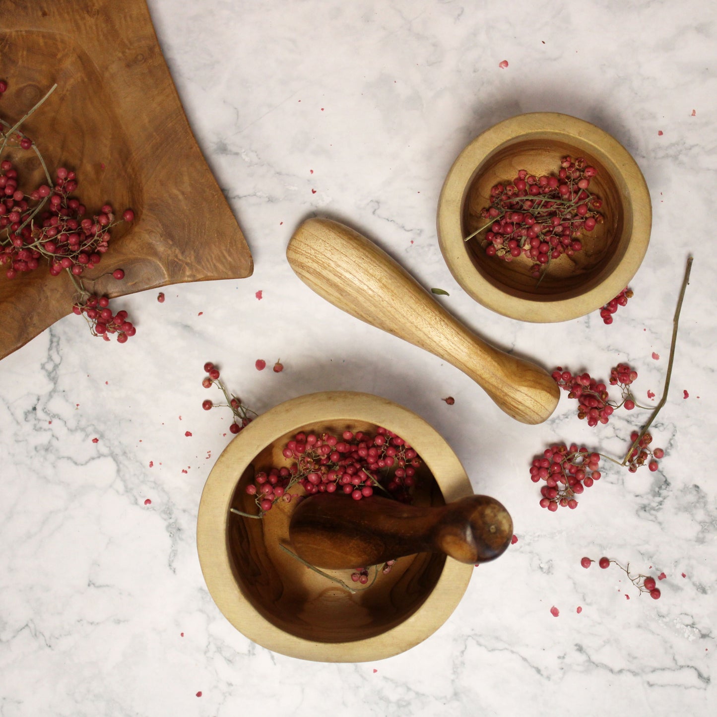 Handgefertigter Mörser mit Stößel aus Teakholz mit rosa Beeren.