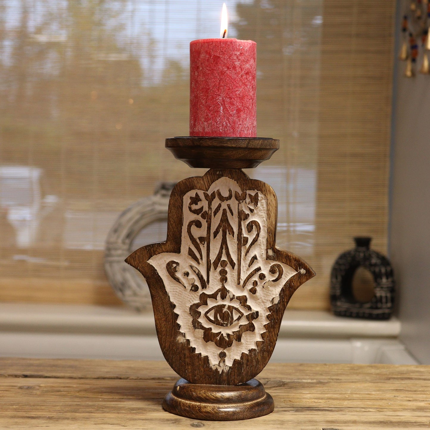 A small, carved mango wood Hamsa hand candle stand holding a red pillar candle.