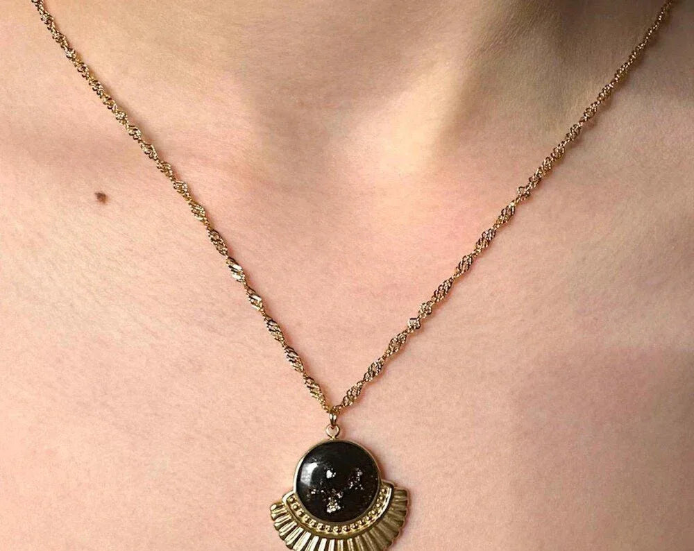 Gold necklace with a dark circular pendant and a fan-shaped gold base.