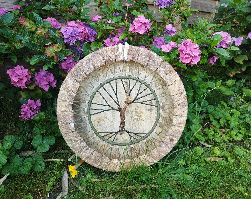 Tunable shamanic drum with a Tree of Life design, set against a backdrop of hydrangeas.