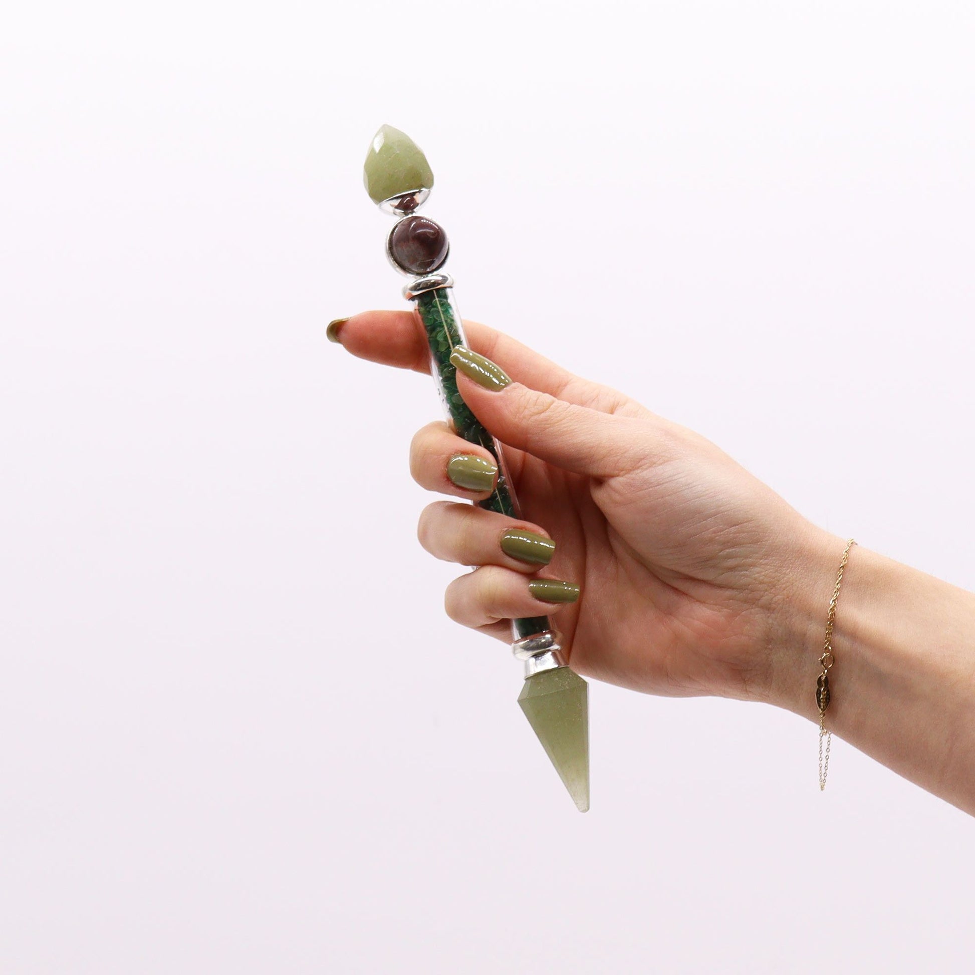 A hand holds a green aventurine magic wand with a pointed tip and decorative stones.