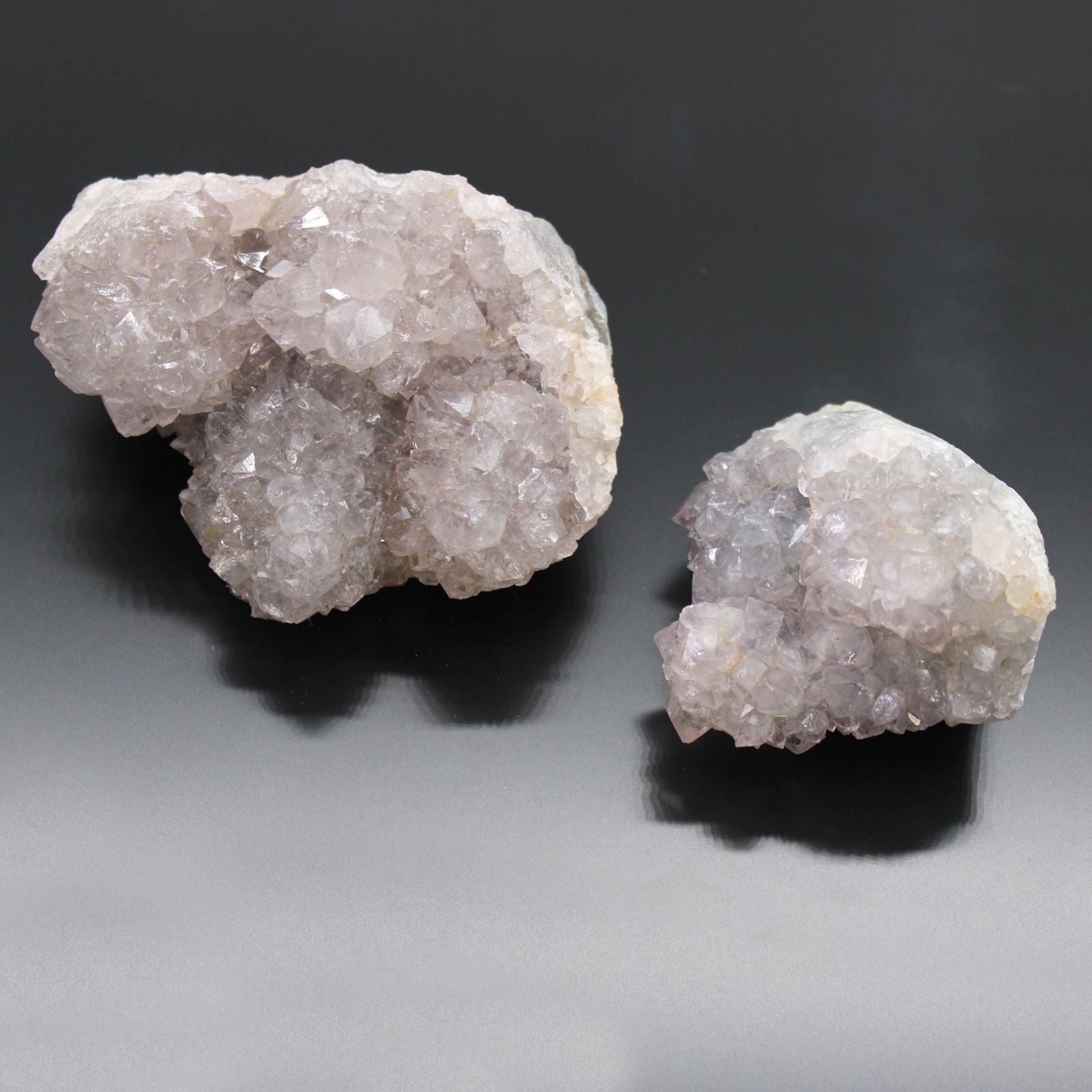 Zwei rohe, naturbelassene Hexenfinger-Quarz-Kristalle auf dunklem Hintergrund.