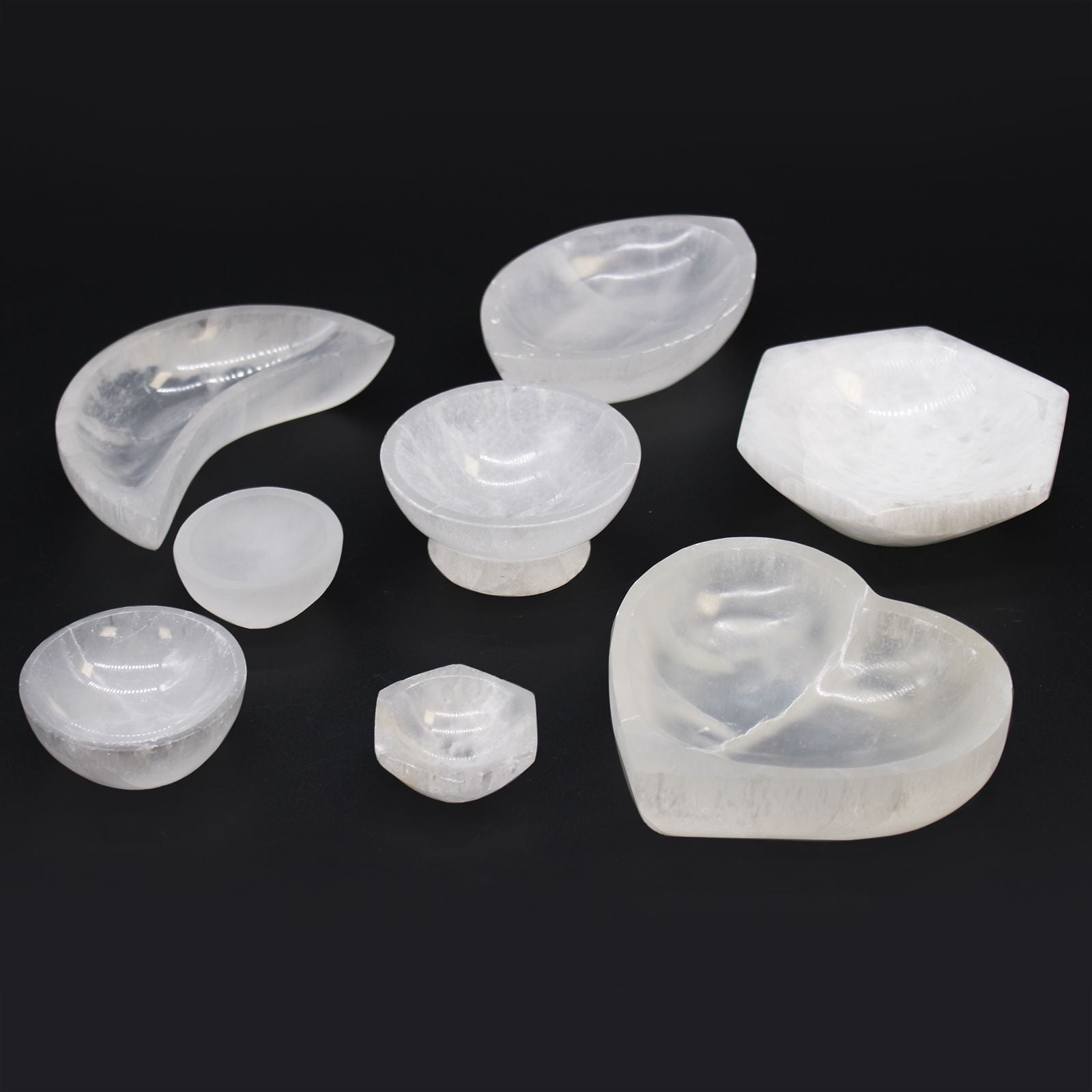 A collection of various white selenite bowls on a black background.