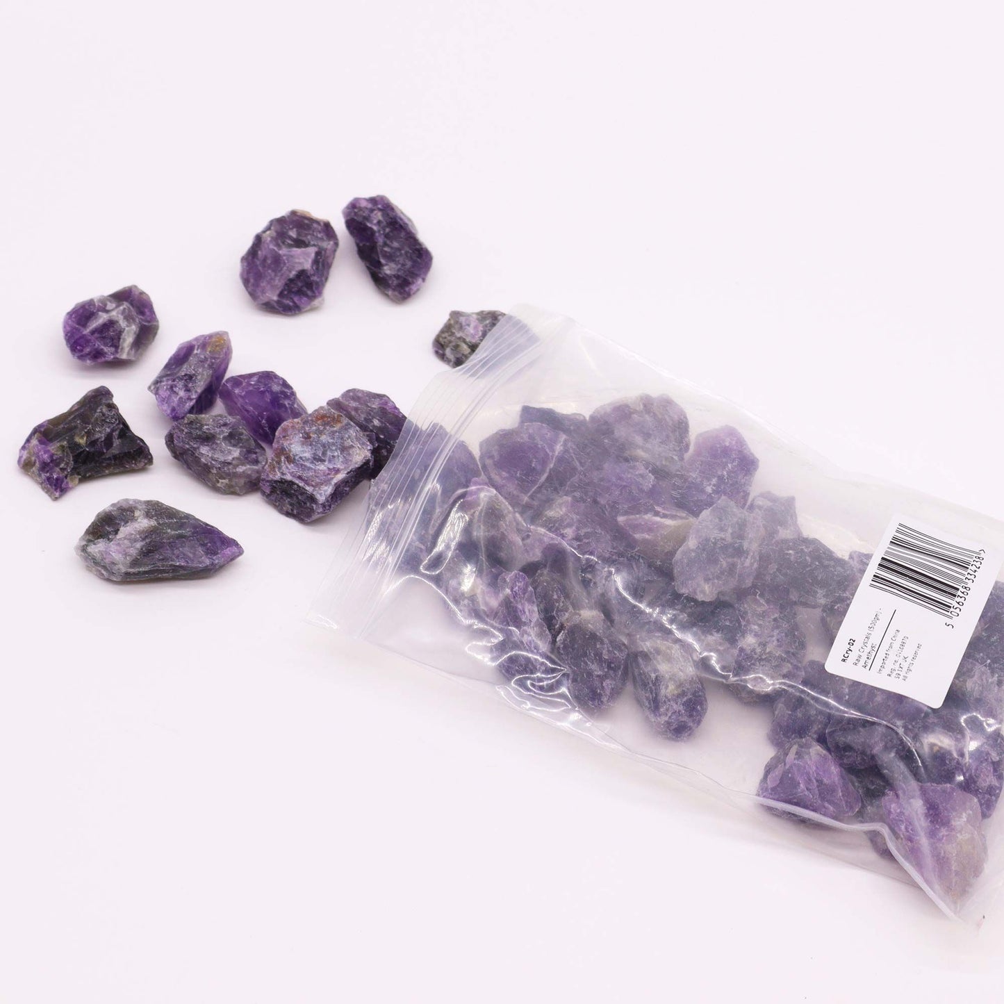 Rohe Amethyst-Rohsteine in einer Plastiktüte und lose auf weißem Hintergrund.