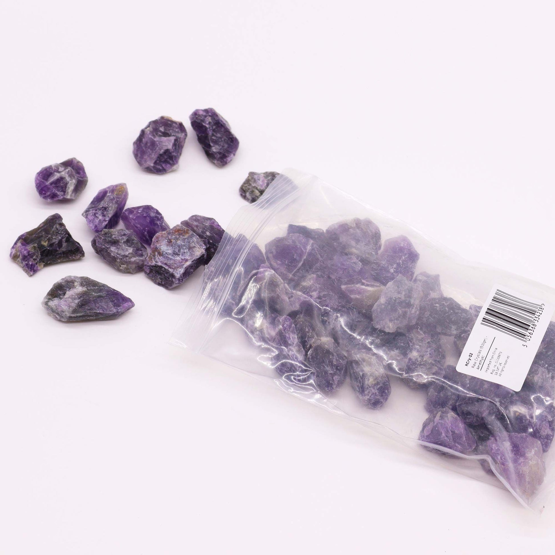 Rohe Amethyst-Rohsteine in einer Plastiktüte und lose auf weißem Hintergrund.