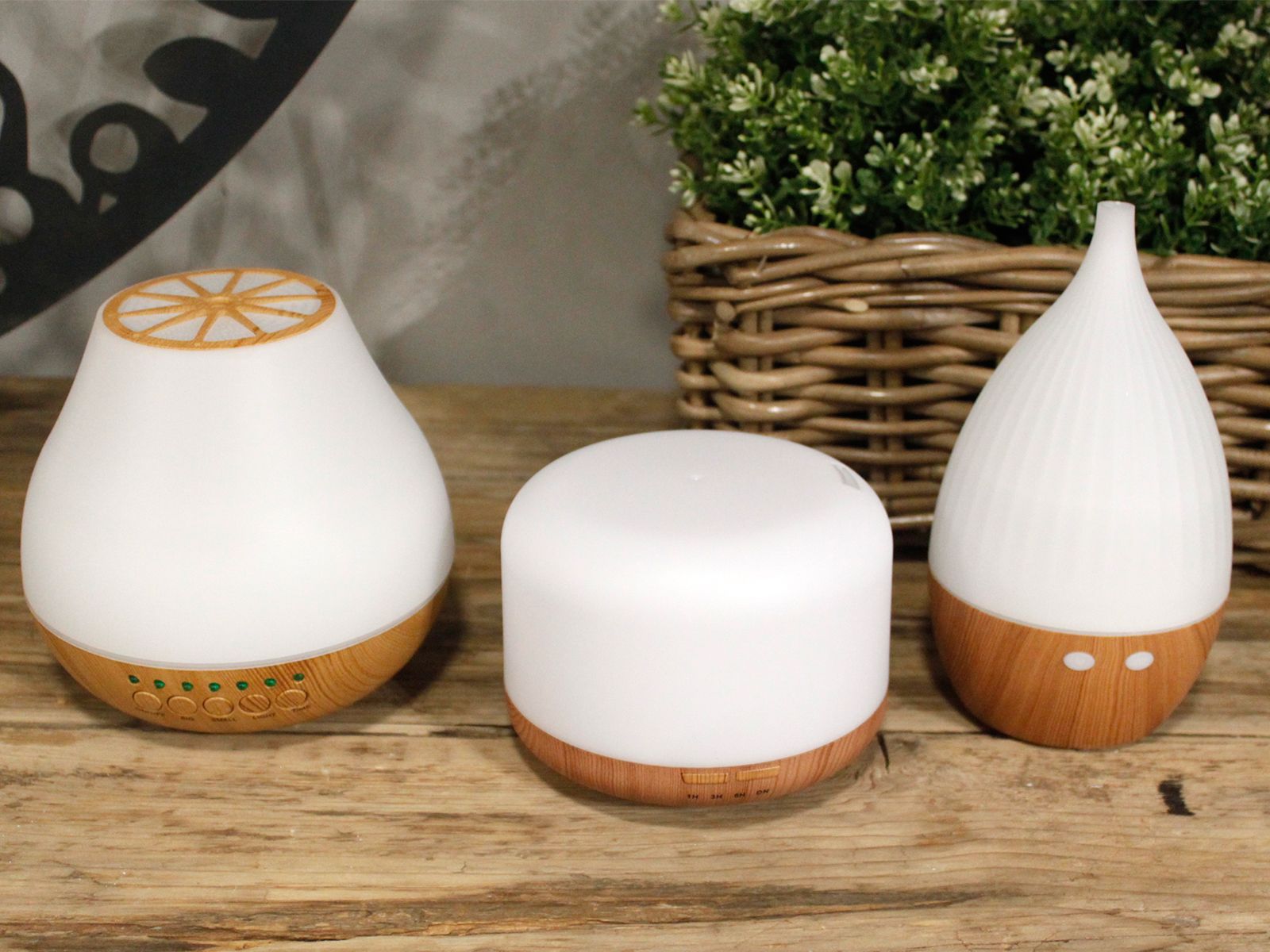 Three white aroma diffusers with wood-grain bases sit on a wooden surface.