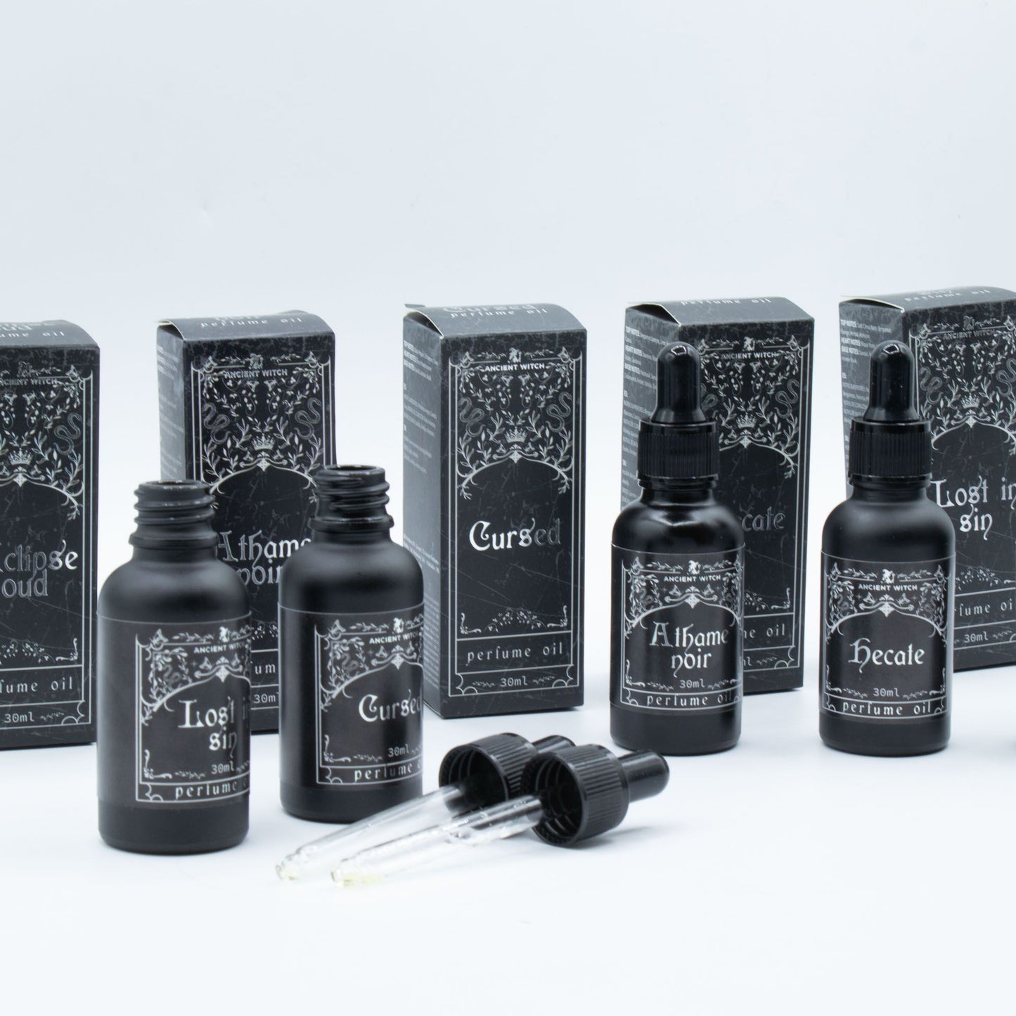 Black bottles of Ancient Witch perfume oil with dropper tops and ornate labels.