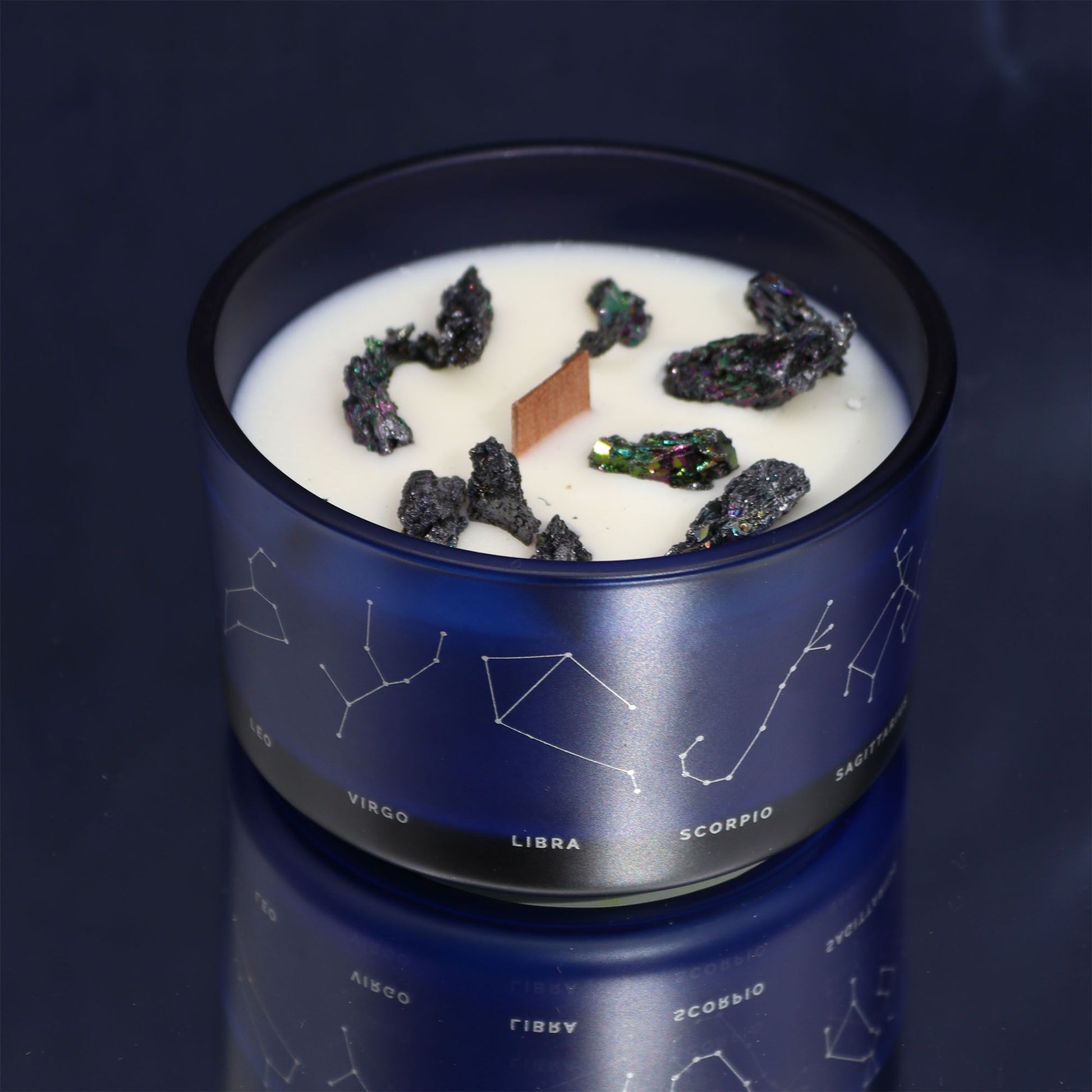 Eine blaue Kerze mit Sternzeichen-Motiv und Kristallen im Wachs.