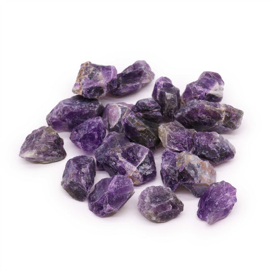 Haufen violetter, ungeschliffener Amethyst-Rohsteine auf weißem Hintergrund.