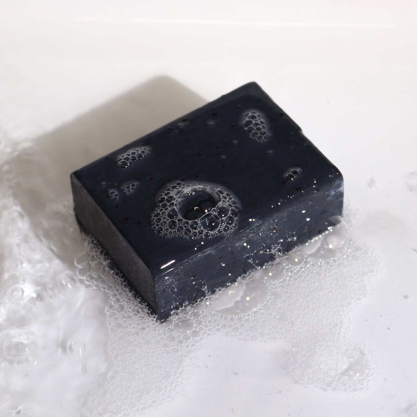 Natürliche Tonerde-Seife mit Aktivkohle und ätherischen Ölen in Wasser mit Schaum.