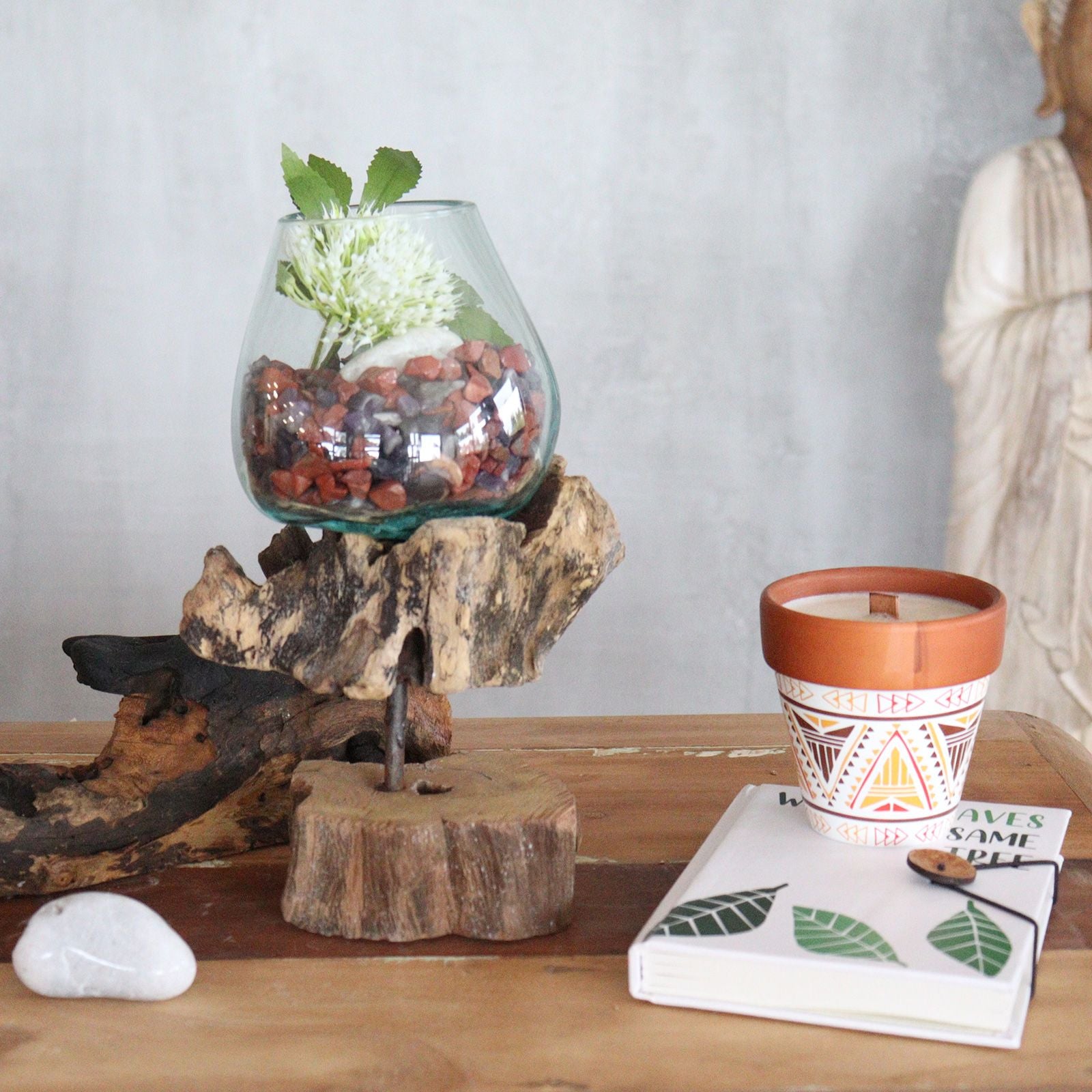 Molten glass bowl with a white flower and stones on a wooden stand.