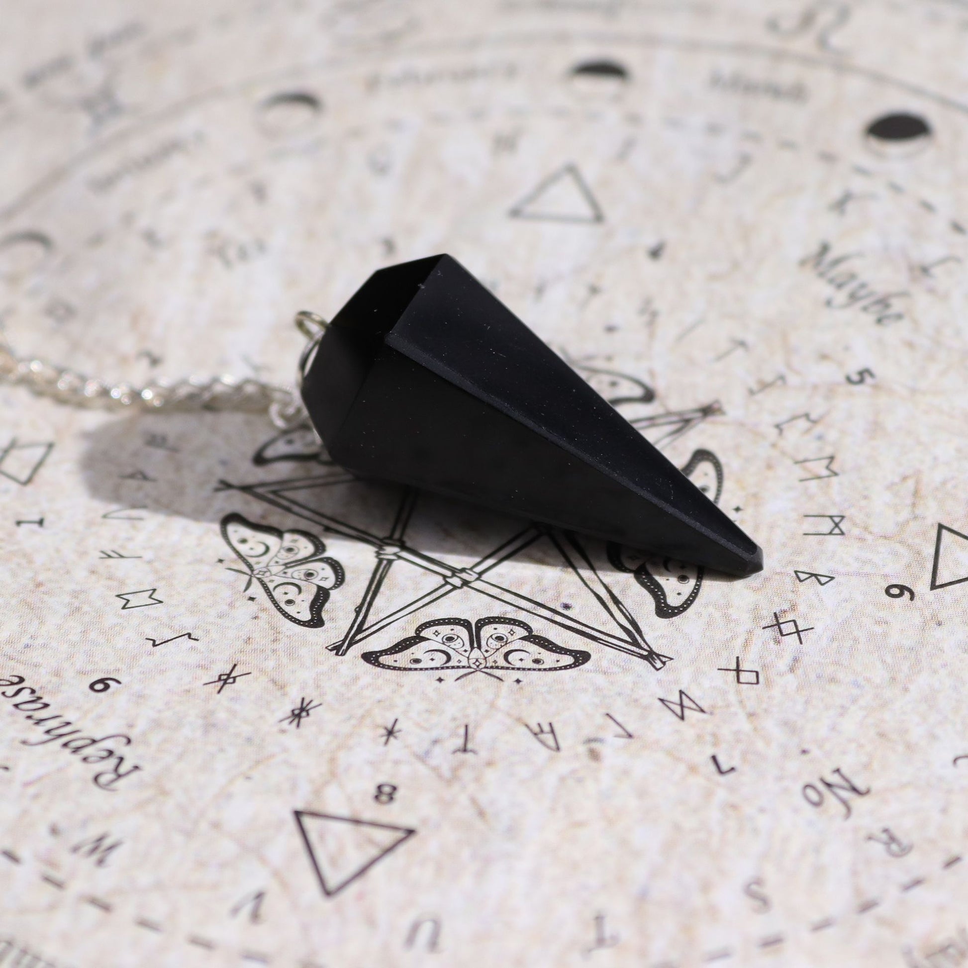 Ein schwarzes Obsidian-Pendel liegt auf einer Pendeltafel mit Symbolen.