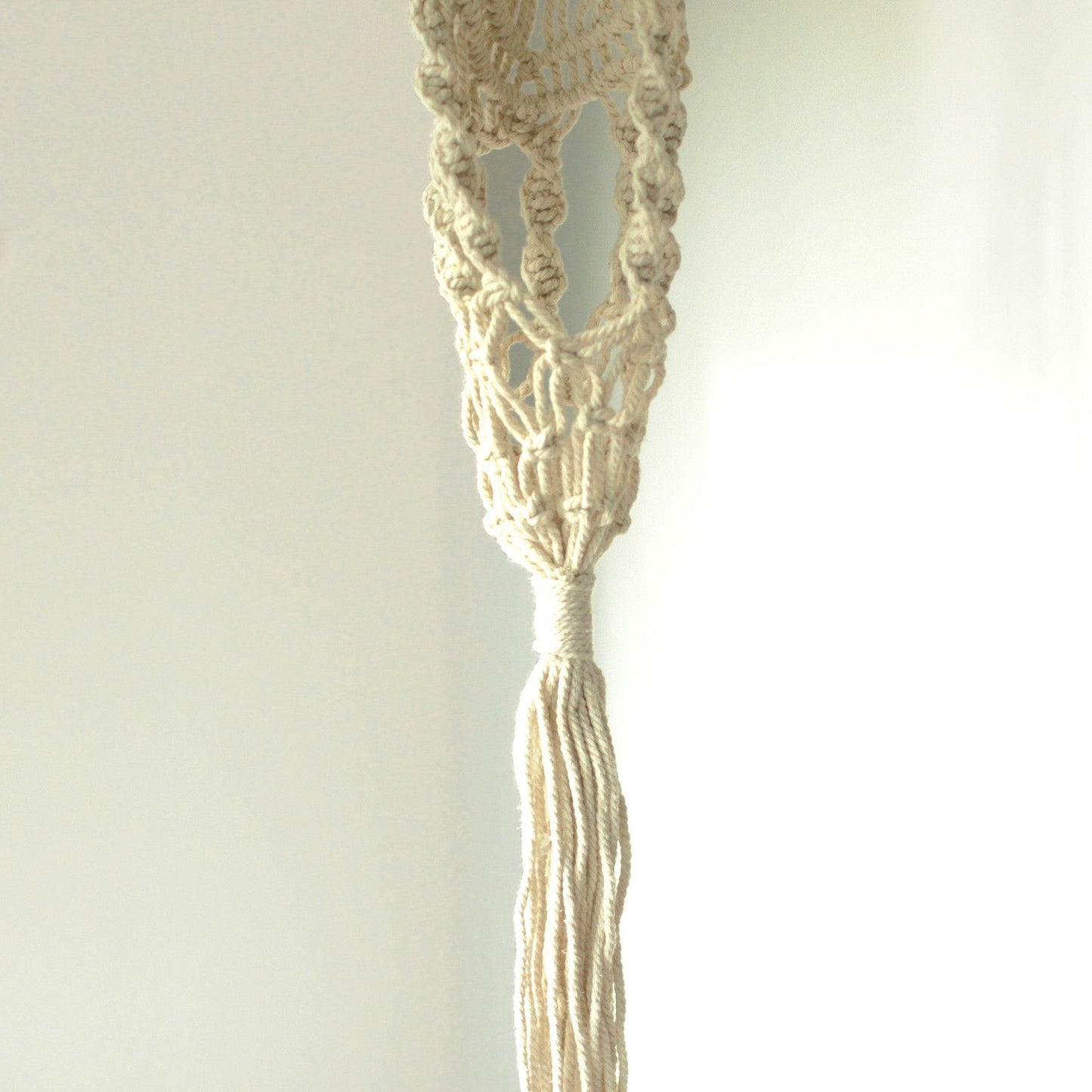 Langer, schmaler Makramee-Blumentopfhalter aus Baumwolle mit Quaste.