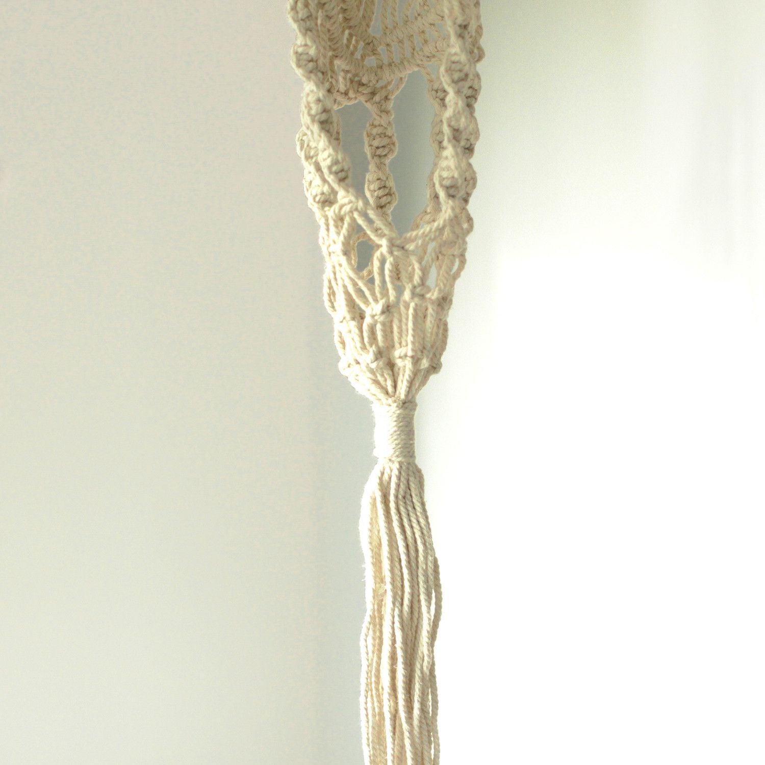 Langer, schmaler Makramee-Blumentopfhalter aus Baumwolle mit Quaste.