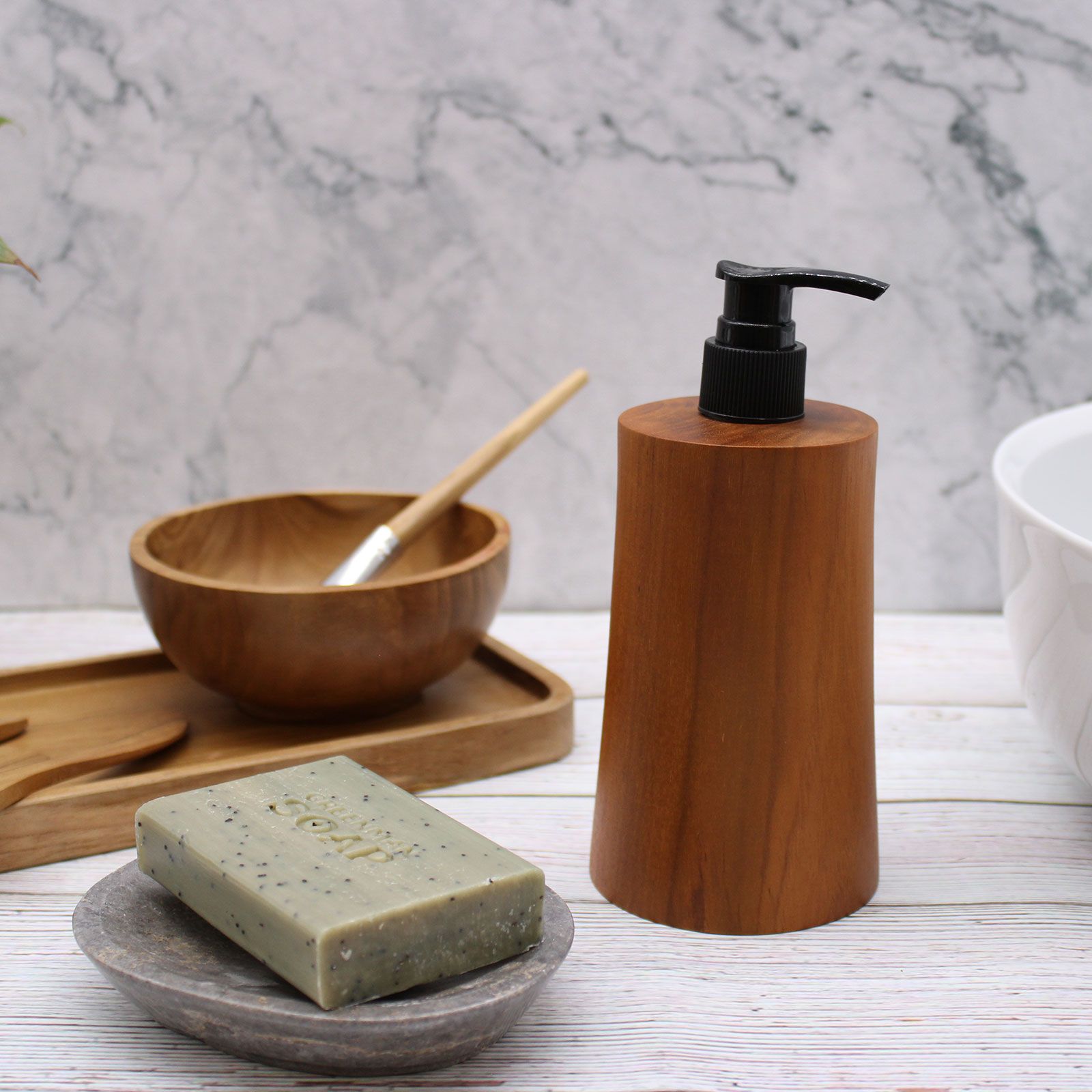 Natural teakwood soap dispenser with a black pump sits next to a bar of green tea soap.