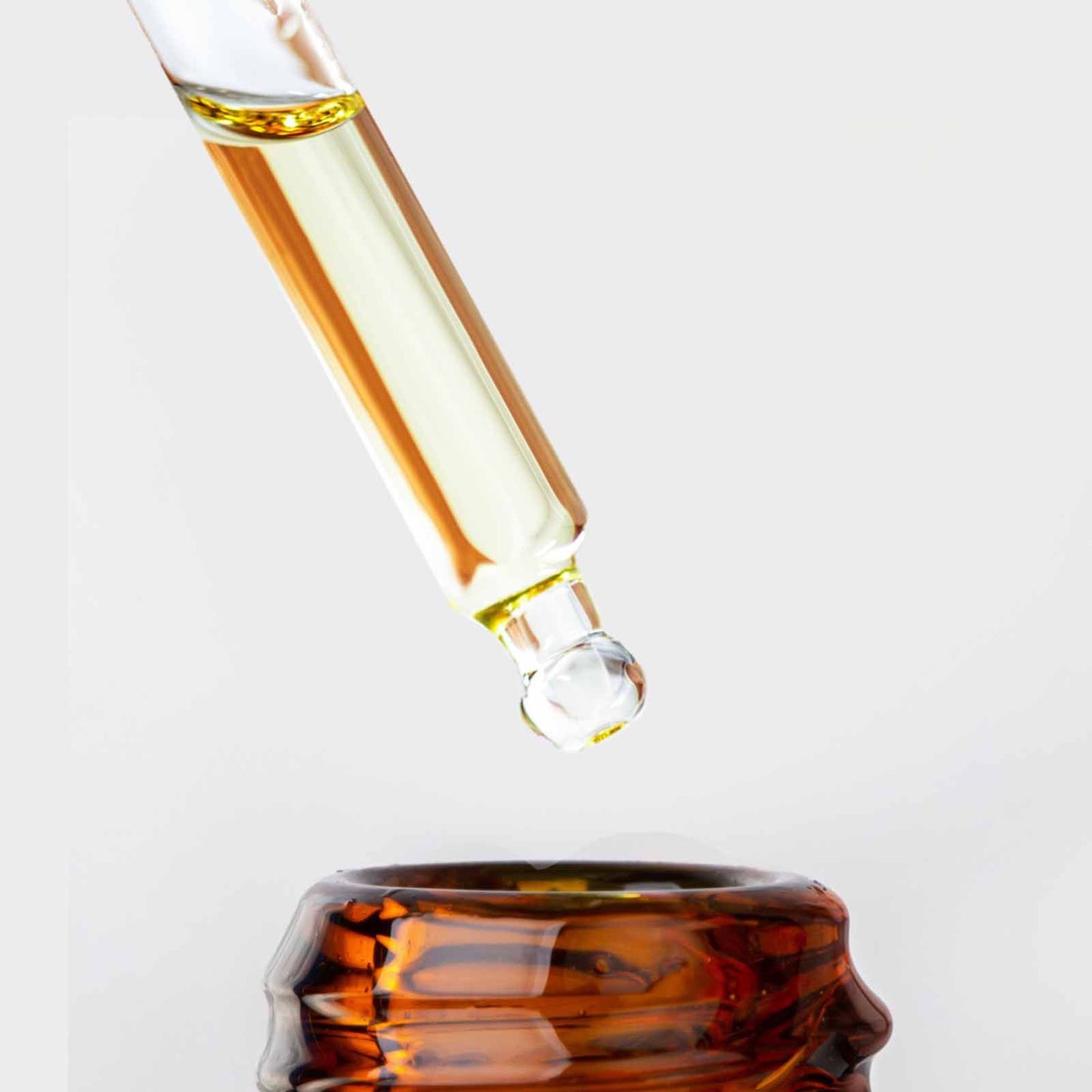 Ein Pipettenfläschchen mit goldenem Serum tropft in eine bernsteinfarbene Flasche.
