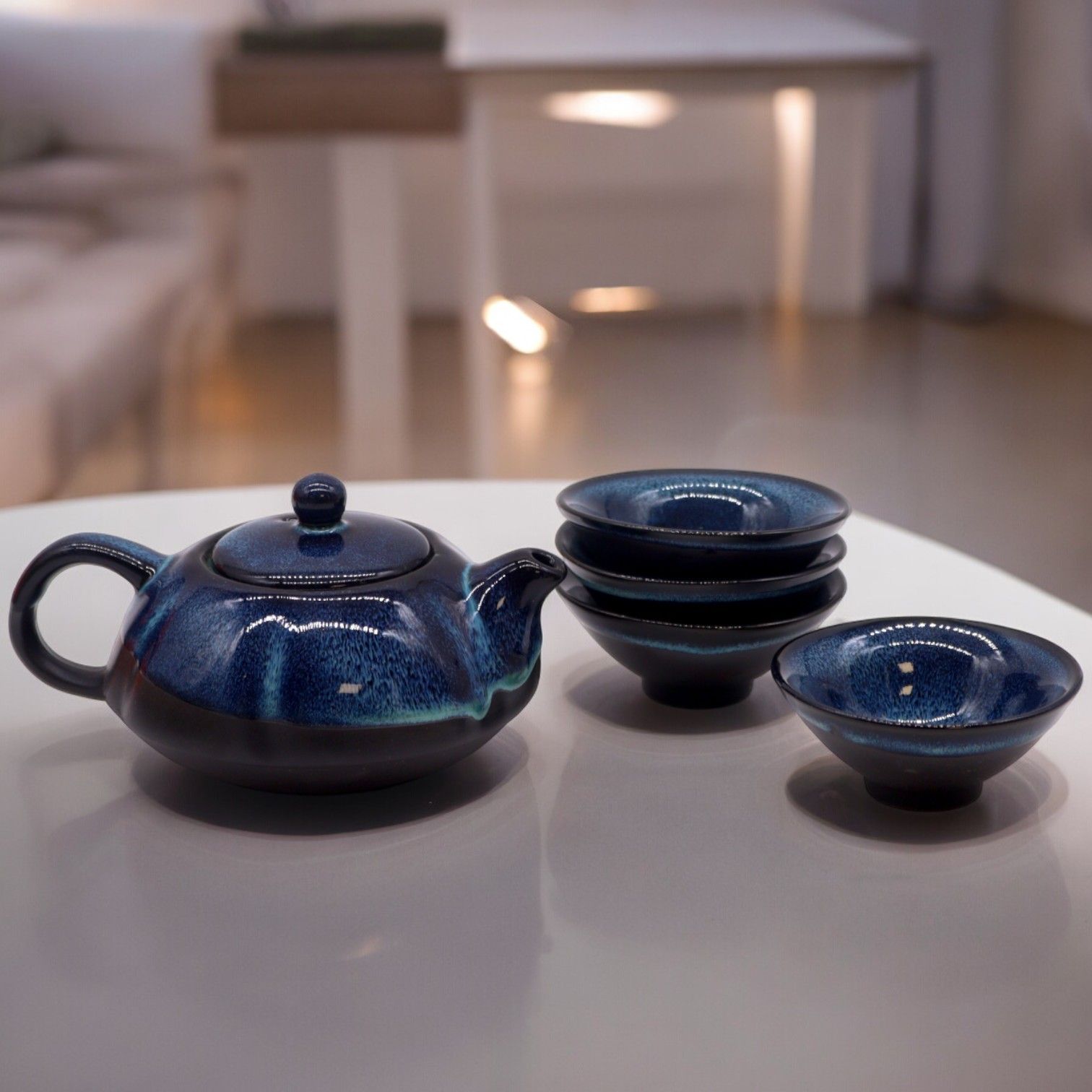 Teekanne und vier blaue Keramiktassen mit glänzender Glasur.
