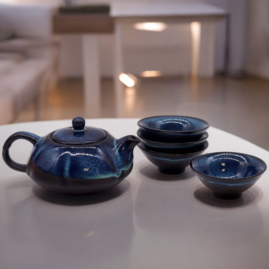 Teekanne und vier blaue Keramiktassen mit glänzender Glasur.