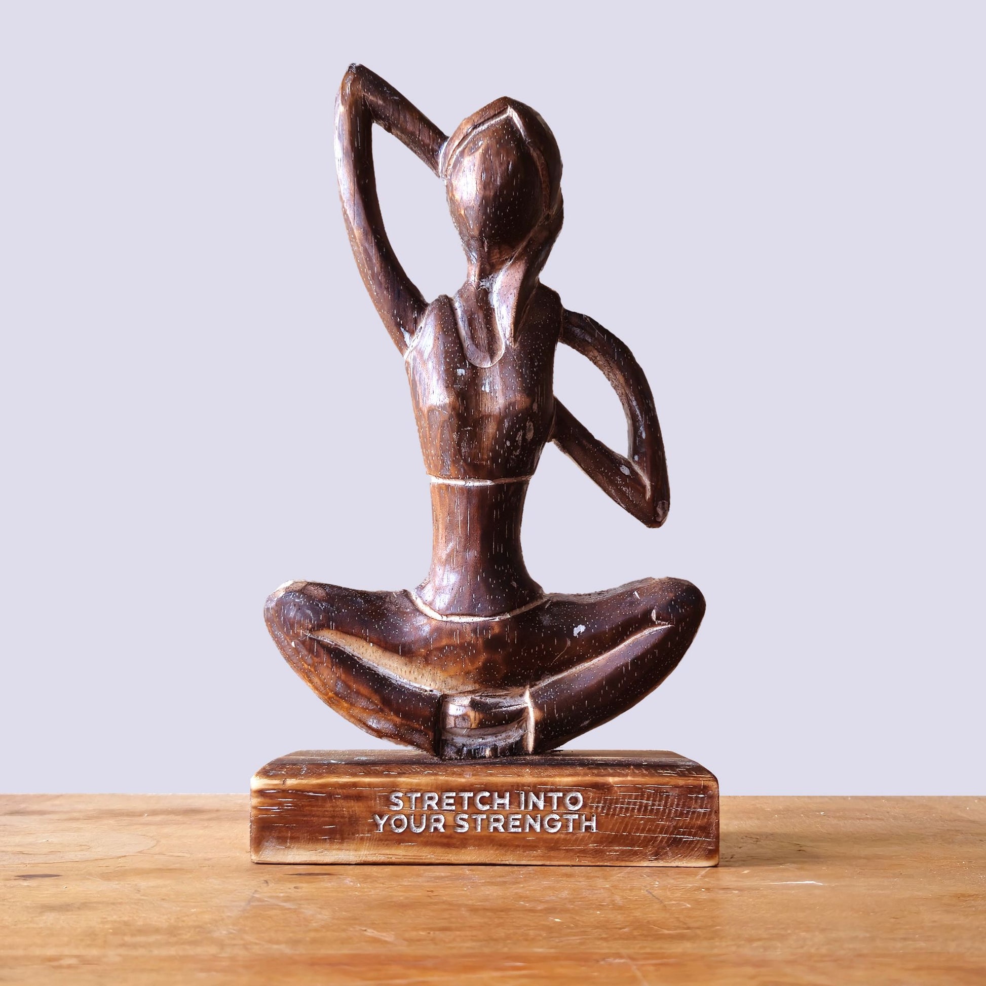 Holzfigur einer Yoga-Praktizierenden mit der Aufschrift "Stretch into Your Strength".