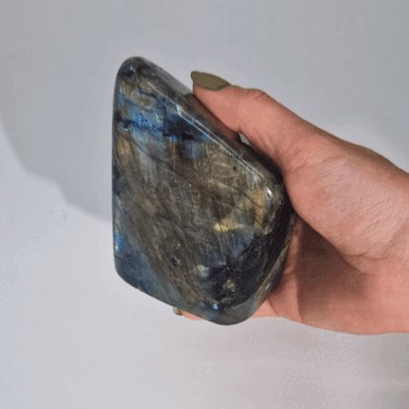 Ein großer, polierter Labradorit mit blau-grünem Schillern in einer Hand.