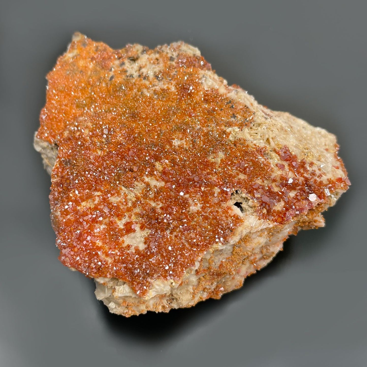 Ein Stück Vanadinit mit leuchtend orange-roten Kristallen auf einer hellen Matrix.
