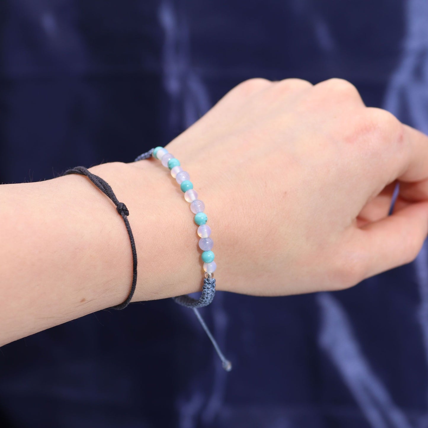 Arm mit zwei Armbändern, eines aus schwarzen Schnur und eines mit blauen und weißen Perlen.