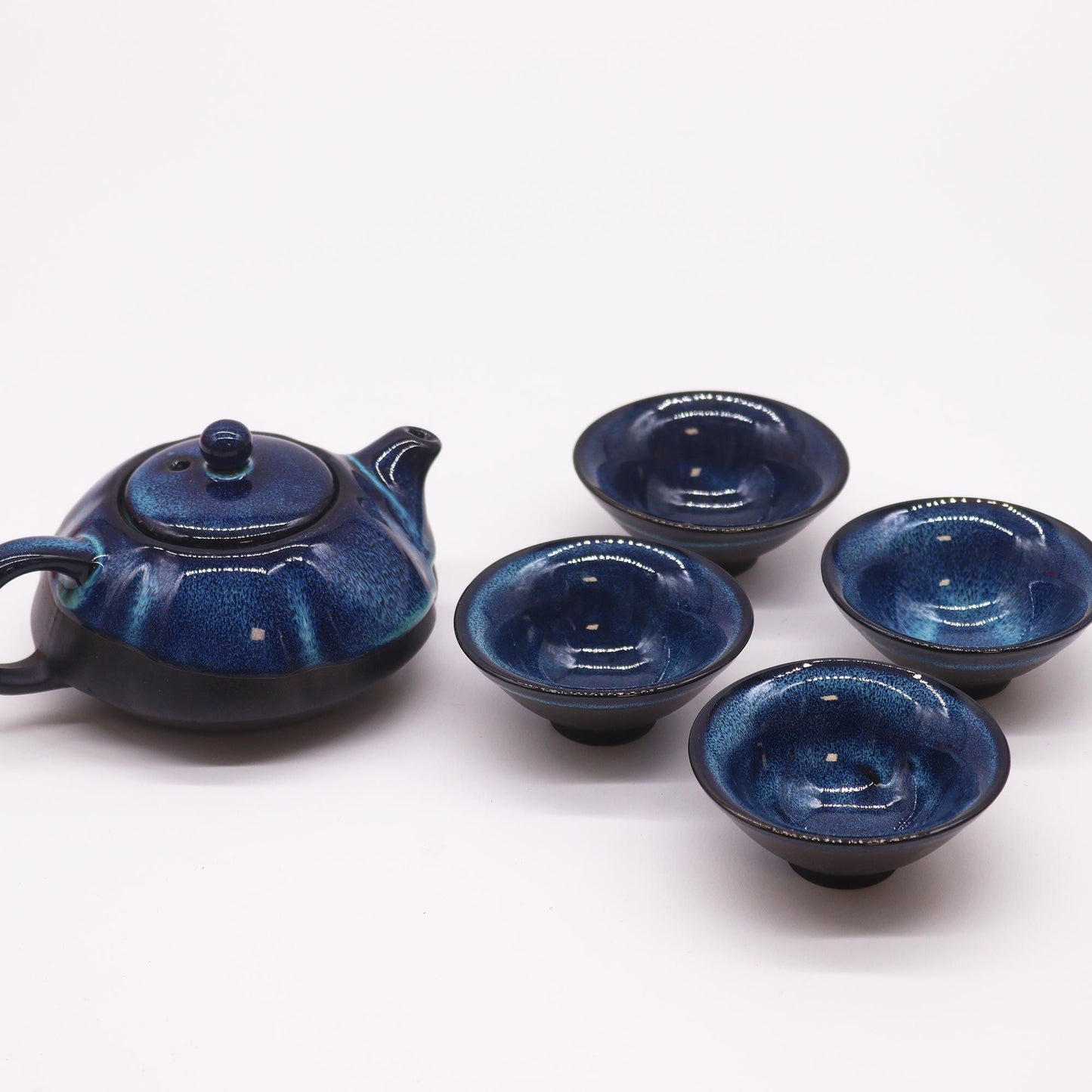 Teekanne und vier blaue Keramiktassen mit glänzender Glasur.