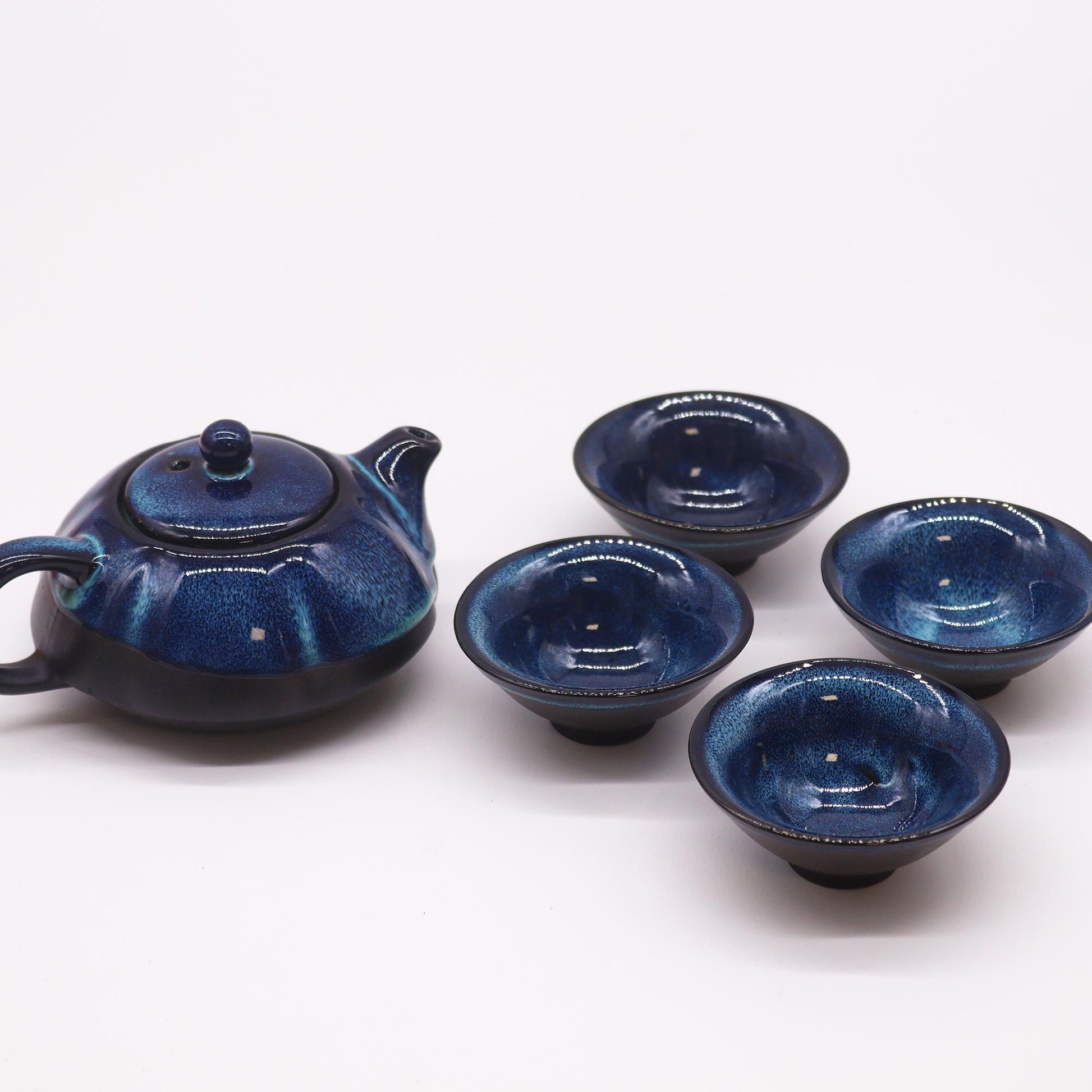 Teekanne und vier blaue Keramiktassen mit glänzender Glasur.