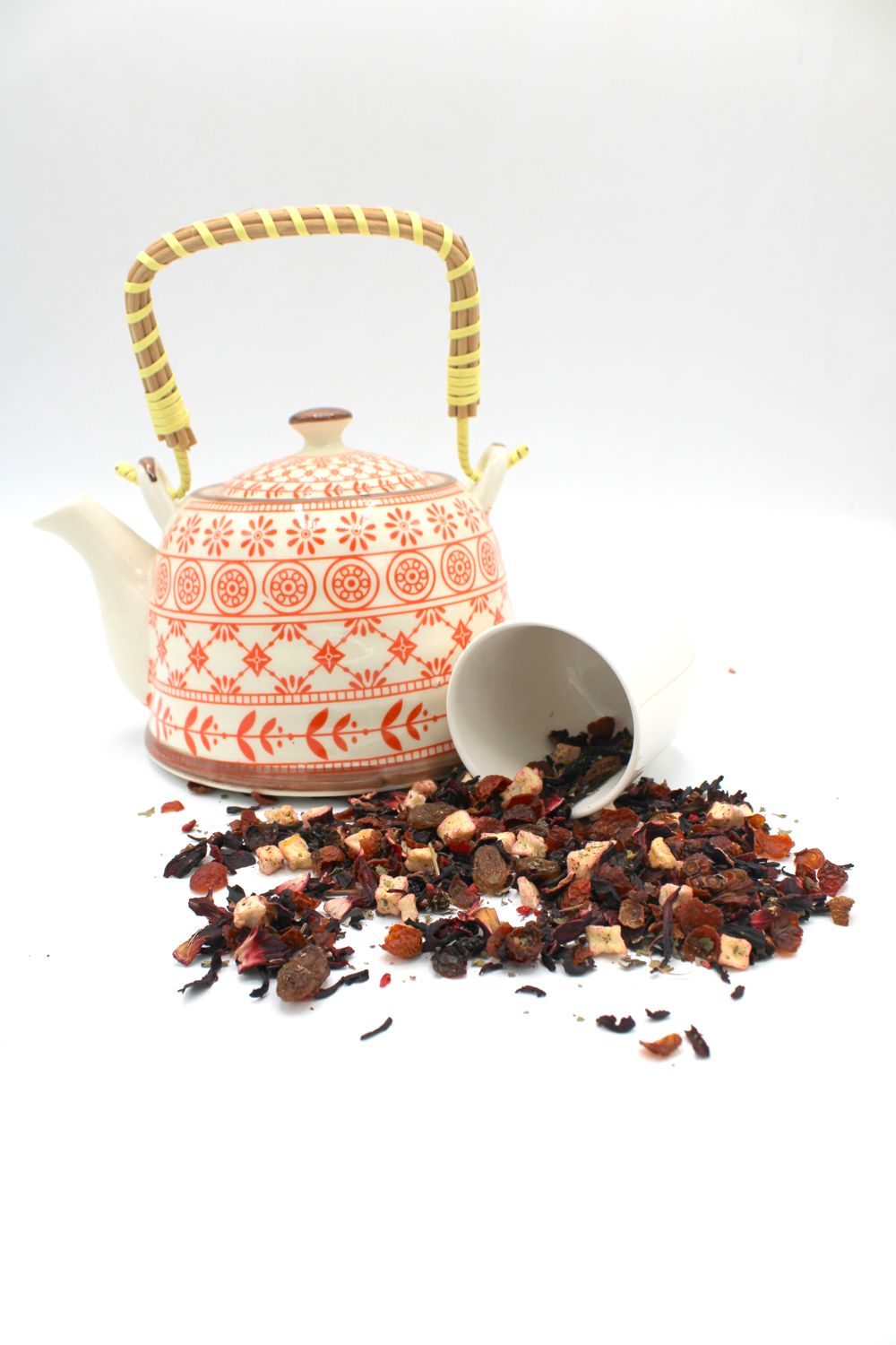A ceramic teapot with a woven handle sits next to a pile of dried fruit and tea leaves.