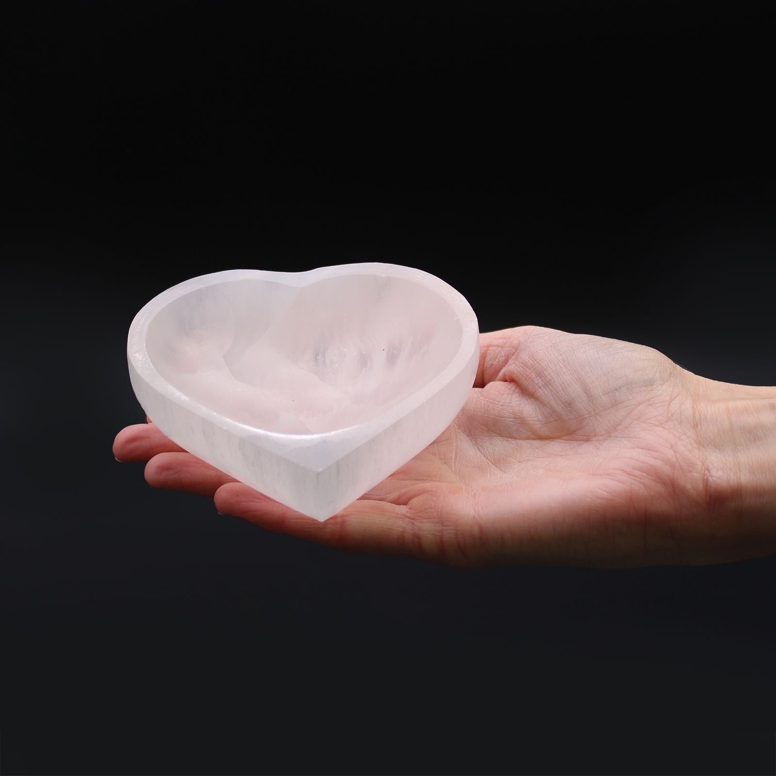 Eine Hand hält eine herzförmige Schale aus weißem Selenit.