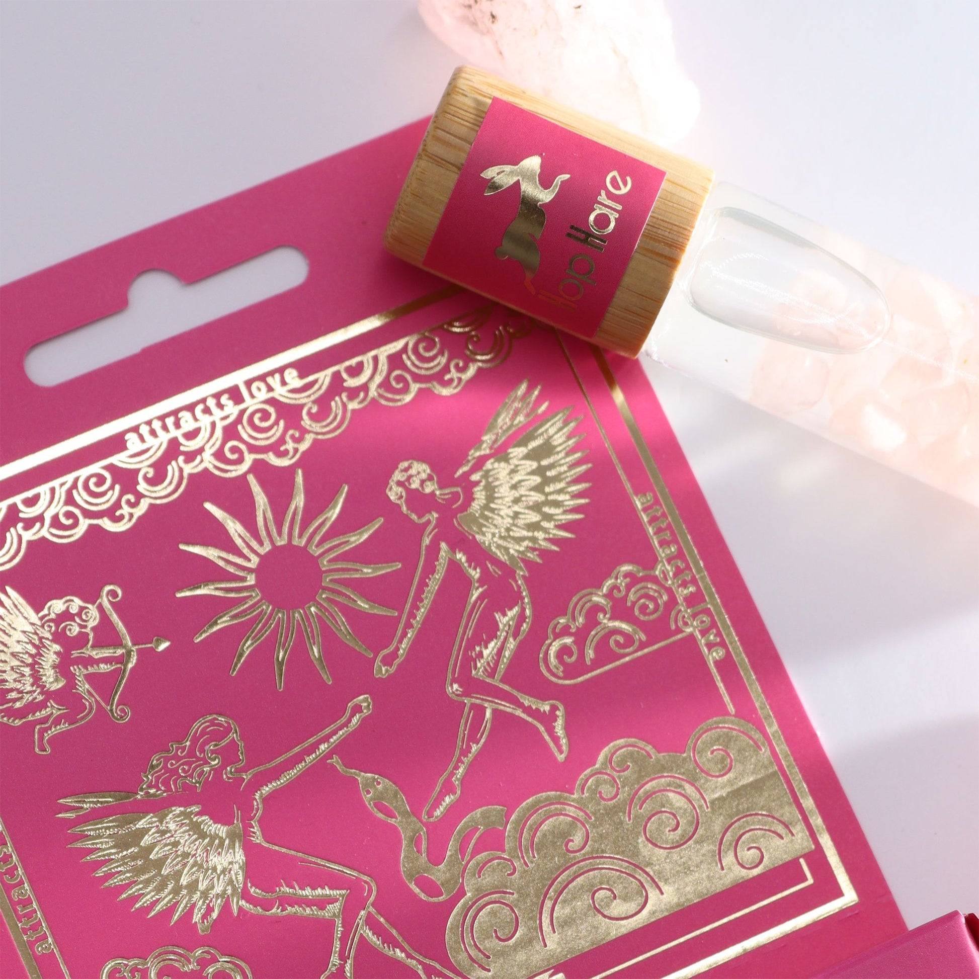 Ein ätherischer Roll-On mit Rosenquarz und Rosenduft auf einer pinken Karte mit goldenen Symbolen.