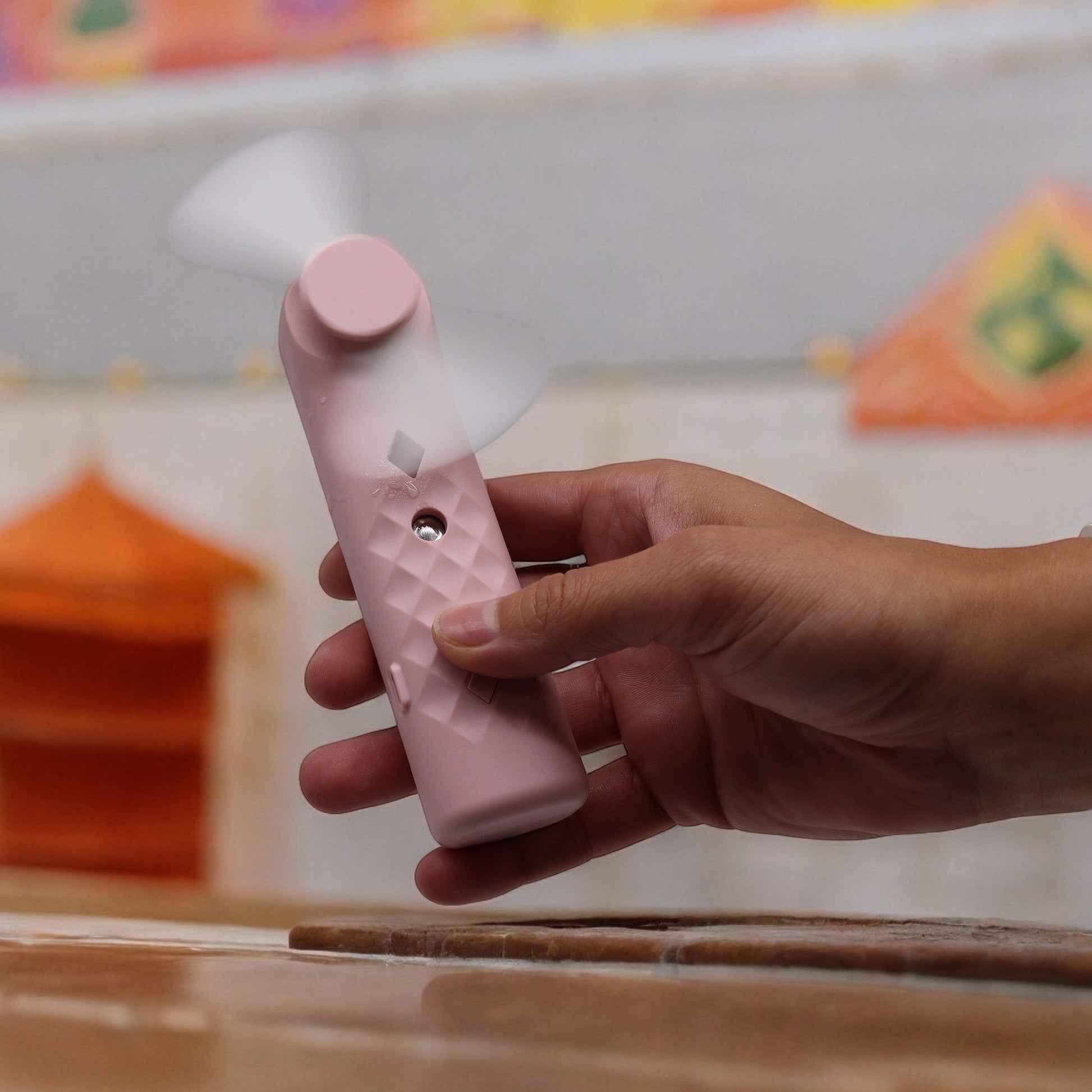 A pink USB rechargeable nano mist face fan and spray held by a hand.