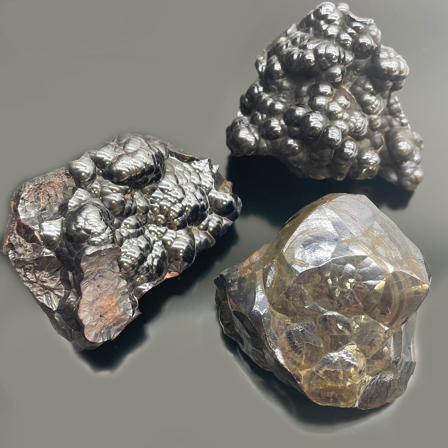 Drei rohe, glänzende Hämatit-Mineralien mit unterschiedlichen Oberflächenstrukturen.