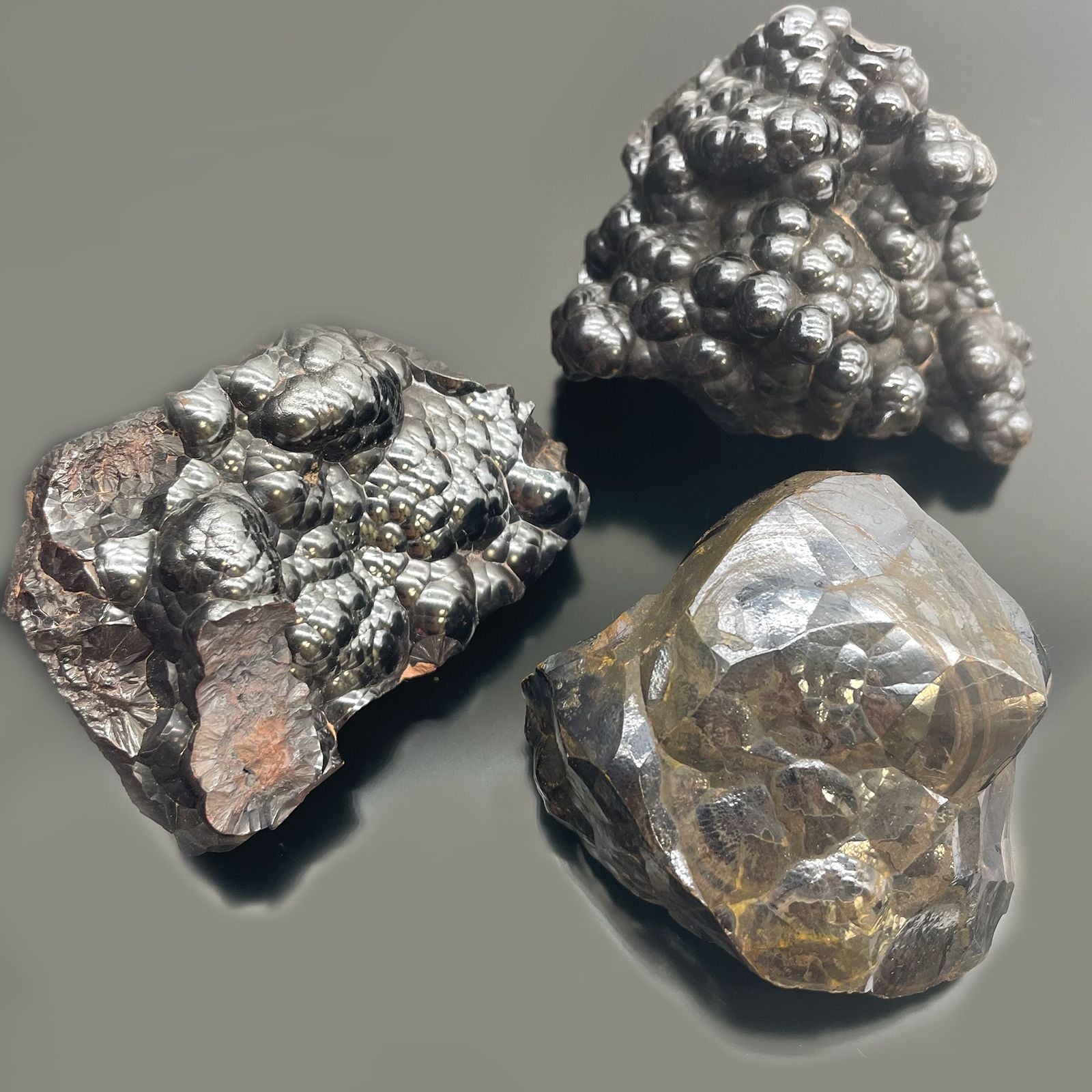 Drei rohe, glänzende Hämatit-Mineralien mit unterschiedlichen Oberflächenstrukturen.