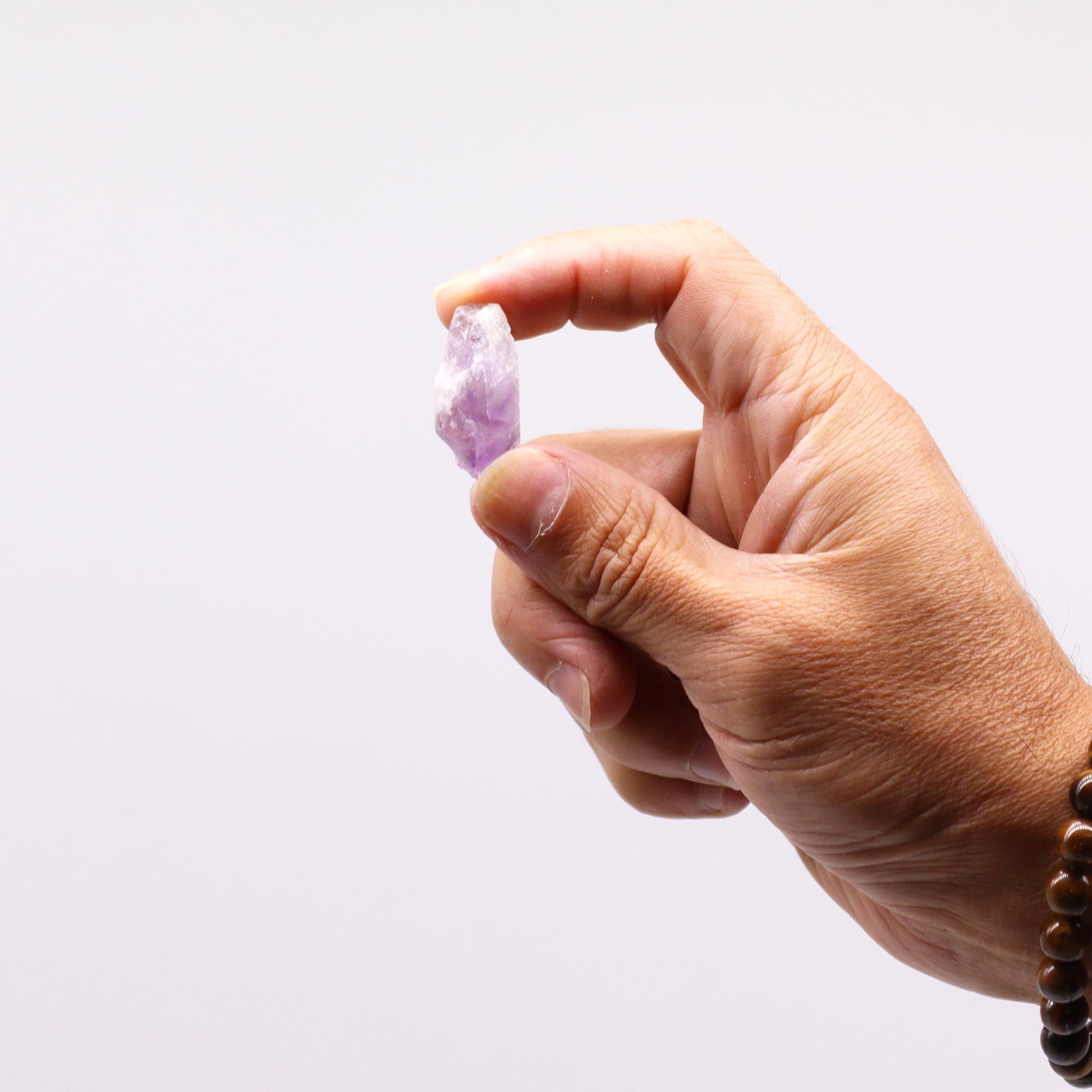 Eine Hand hält eine kleine, rohe, violette Amethyst-Kristallspitze.
