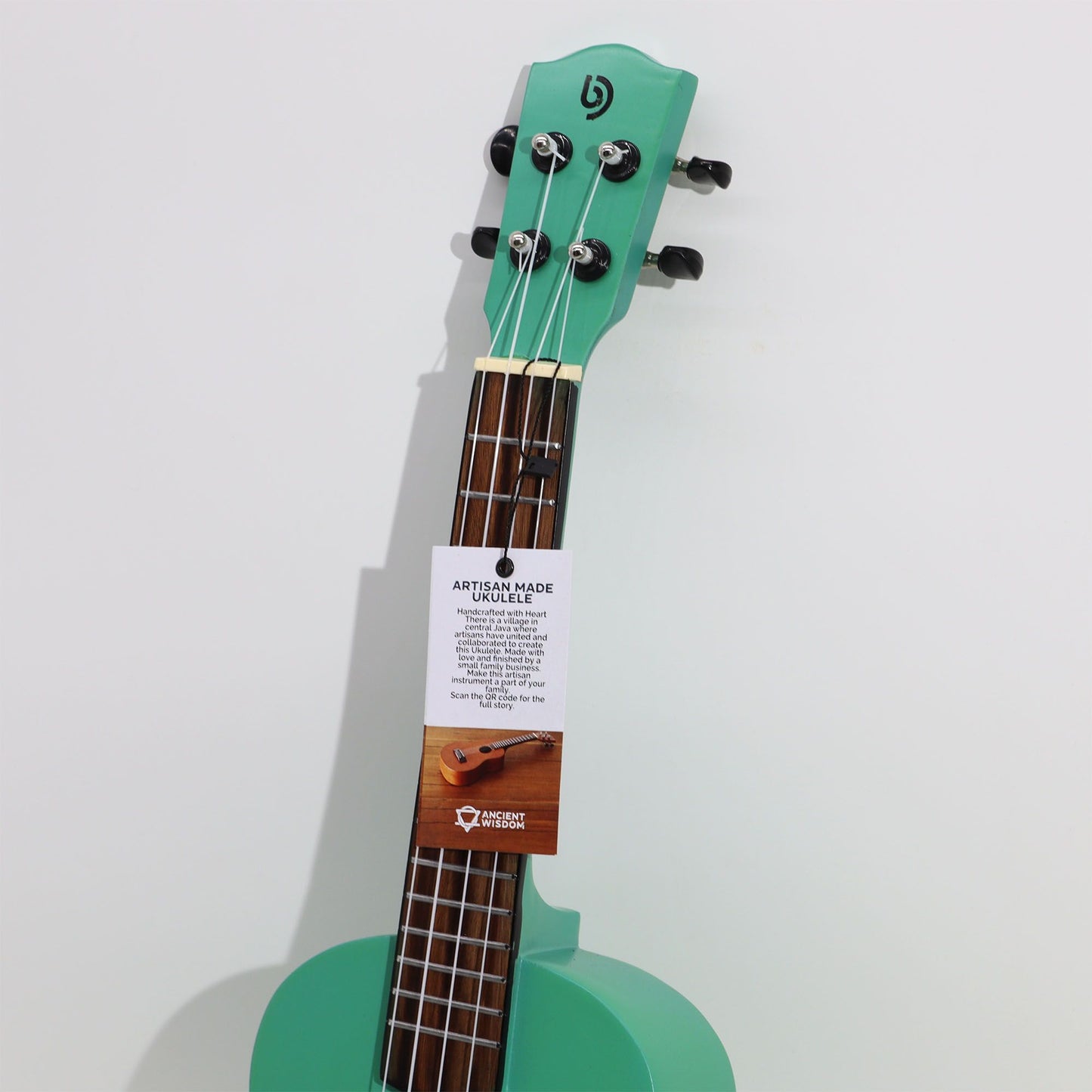 Eine türkisfarbene Ukulele mit einem Anhänger, der die Handwerkskunst hervorhebt.