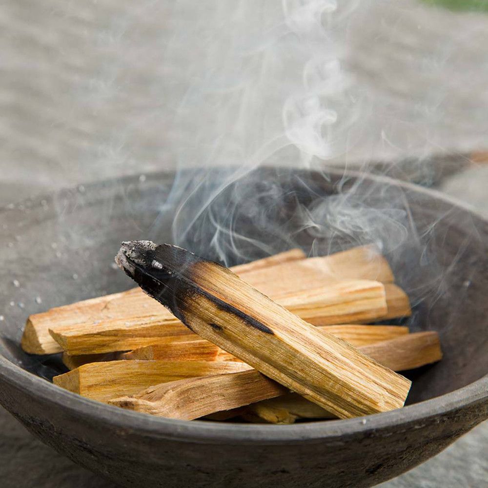 Palo Santo Räucherstäbchen in einer Schale mit aufsteigendem Rauch.