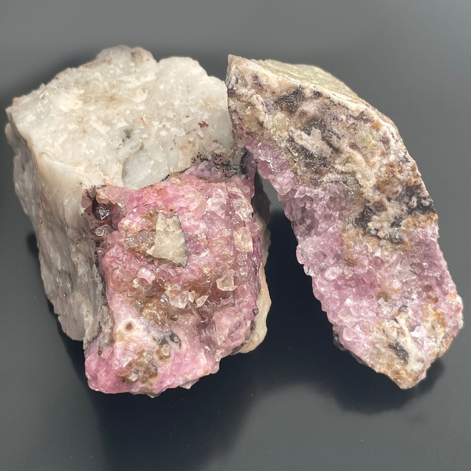 Drei rohe Kobalt-Calcit-Steine in Rosa- und Violetttönen auf schwarzem Hintergrund.