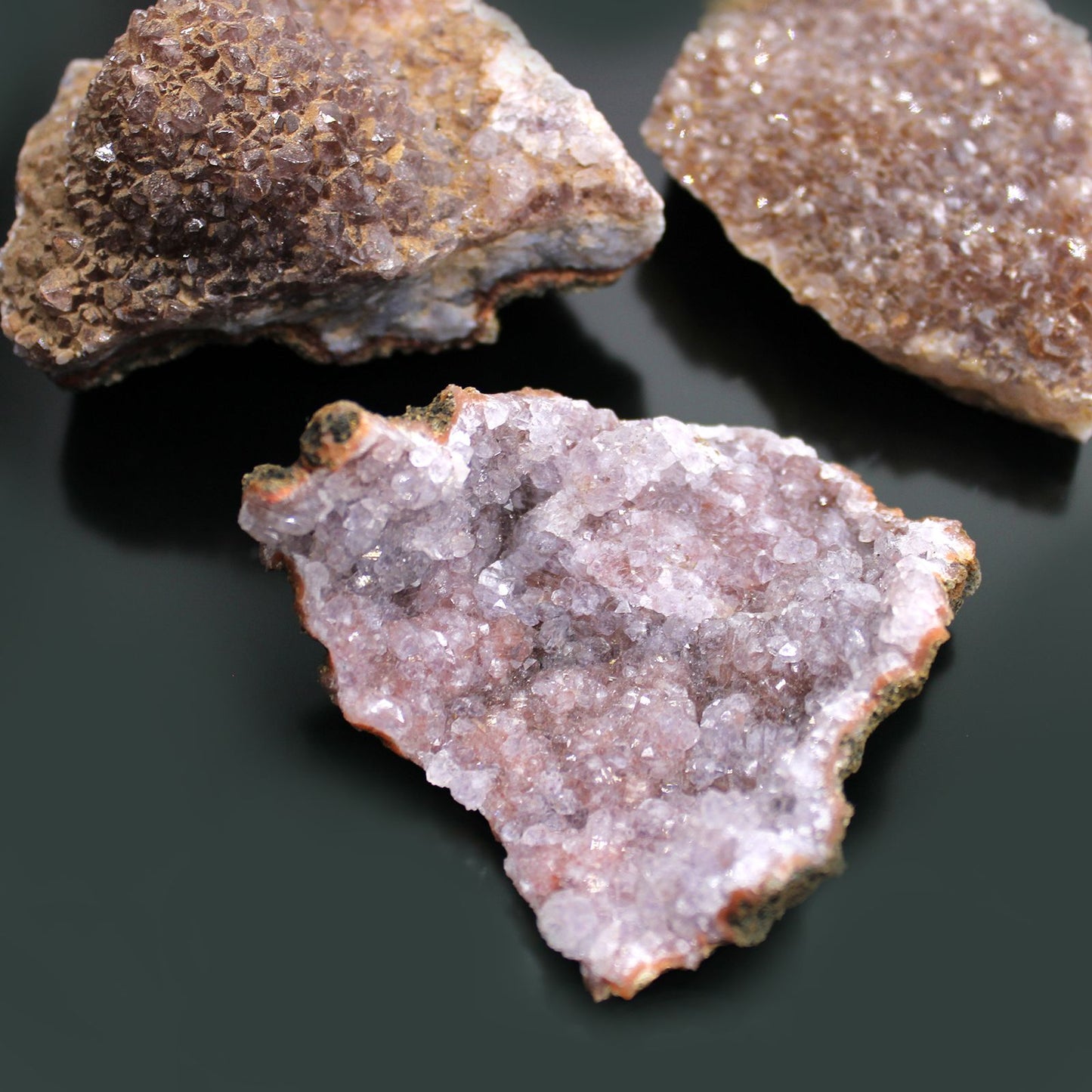 Drei rohe Amethyst-Geoden mit violetten Kristallen auf dunklem Hintergrund.
