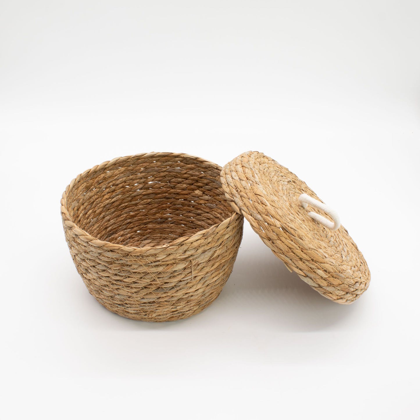 A natural seagrass round basket with a lid and white loop handle.